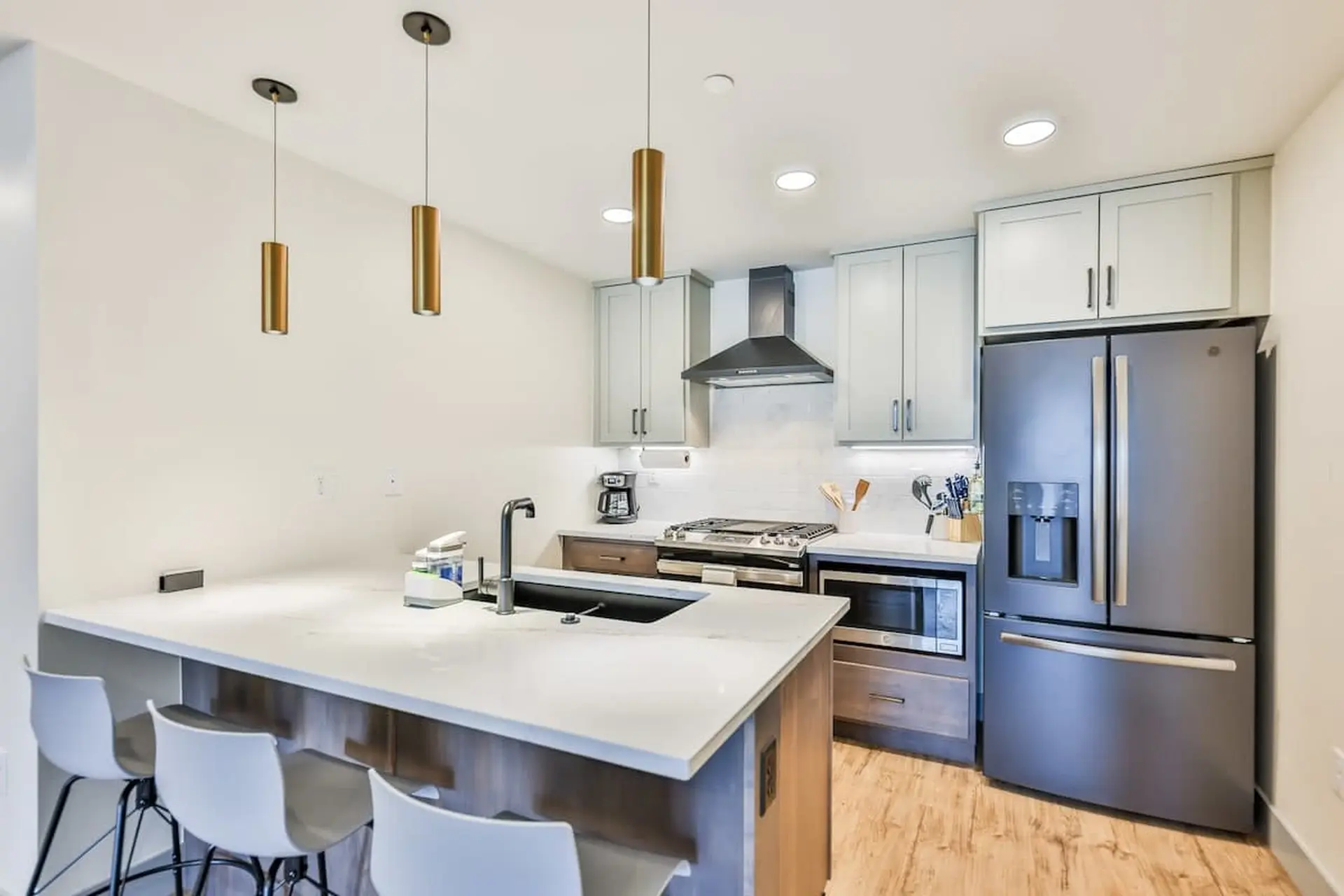 A modern kitchen with a gray refrigerator, light gray cabinets, and a large island.