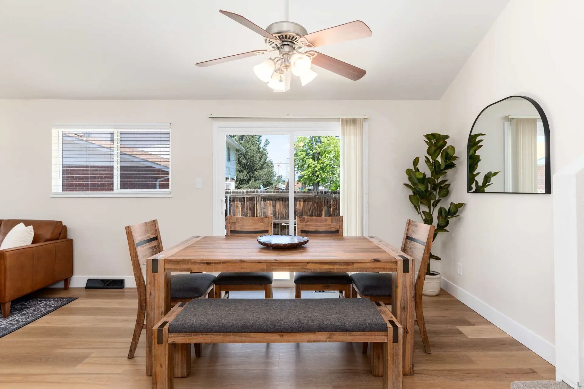 A dining room with a wooden table and chairs, a ceiling fan, and a large plant.