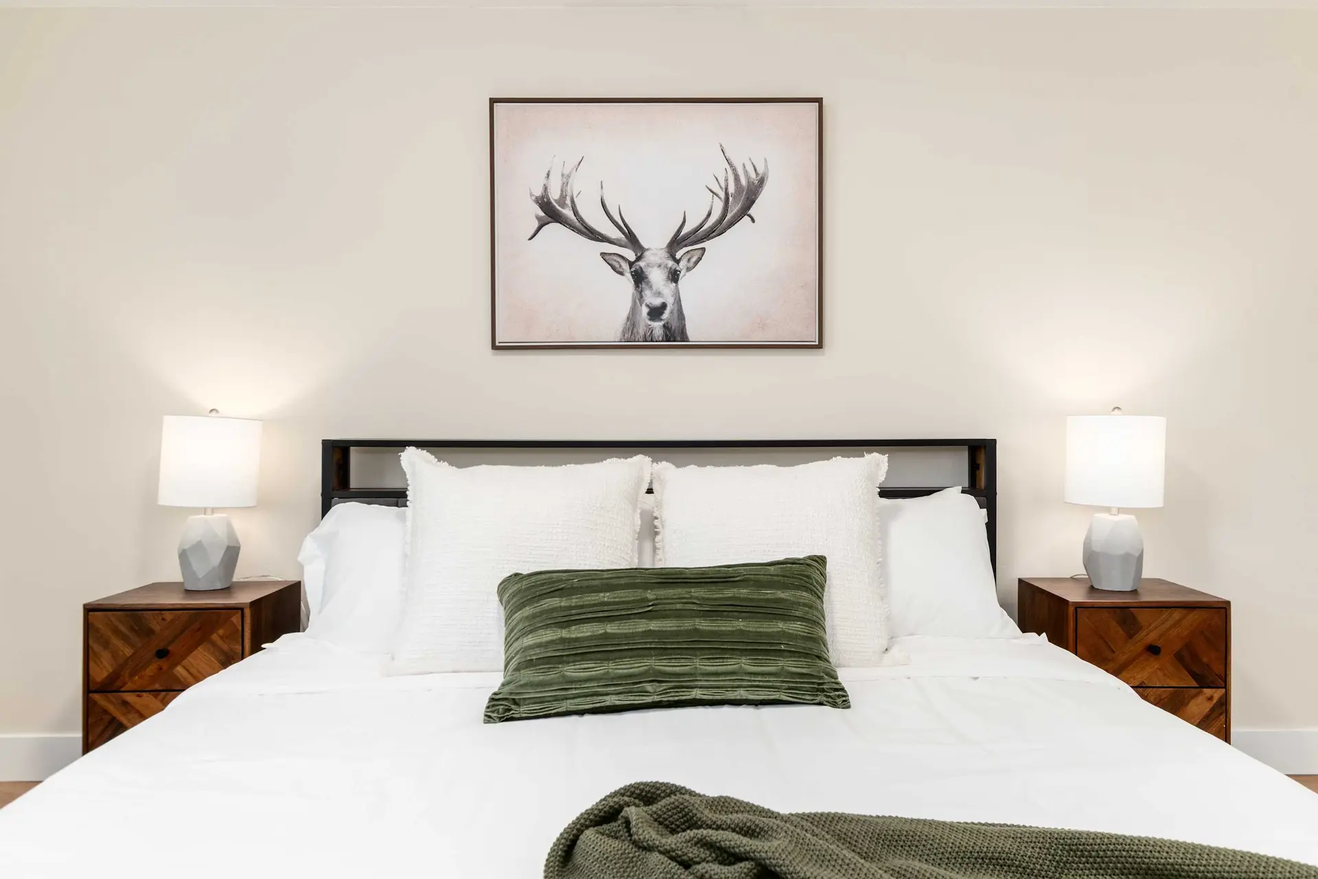 A bed with white bedding, a green pillow, and a deer artwork above.