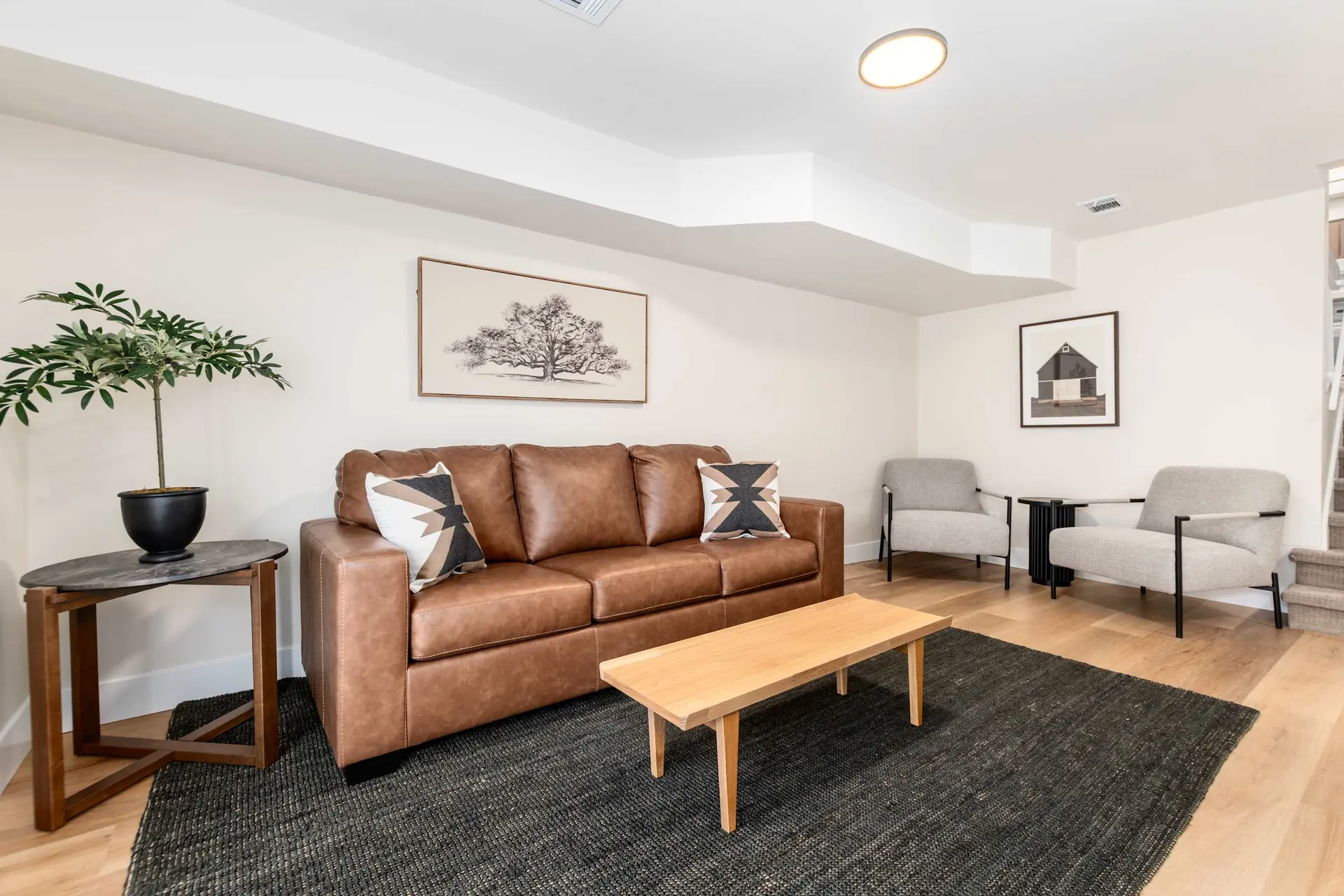 A living room with a brown leather sofa, two armchairs, a coffee table, and a large rug.