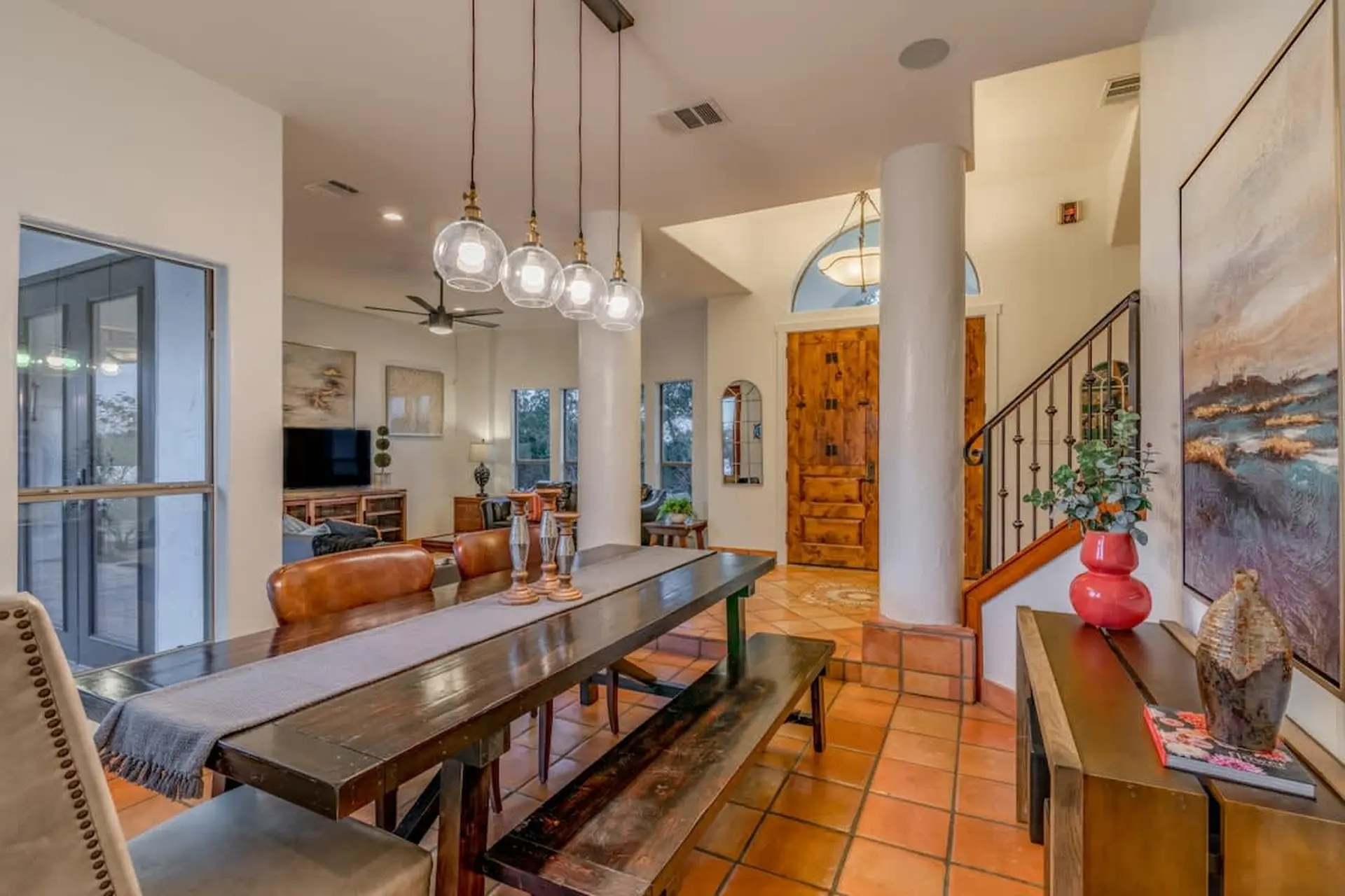 A dining area with a long wooden table and bench, illuminated by pendant lights.