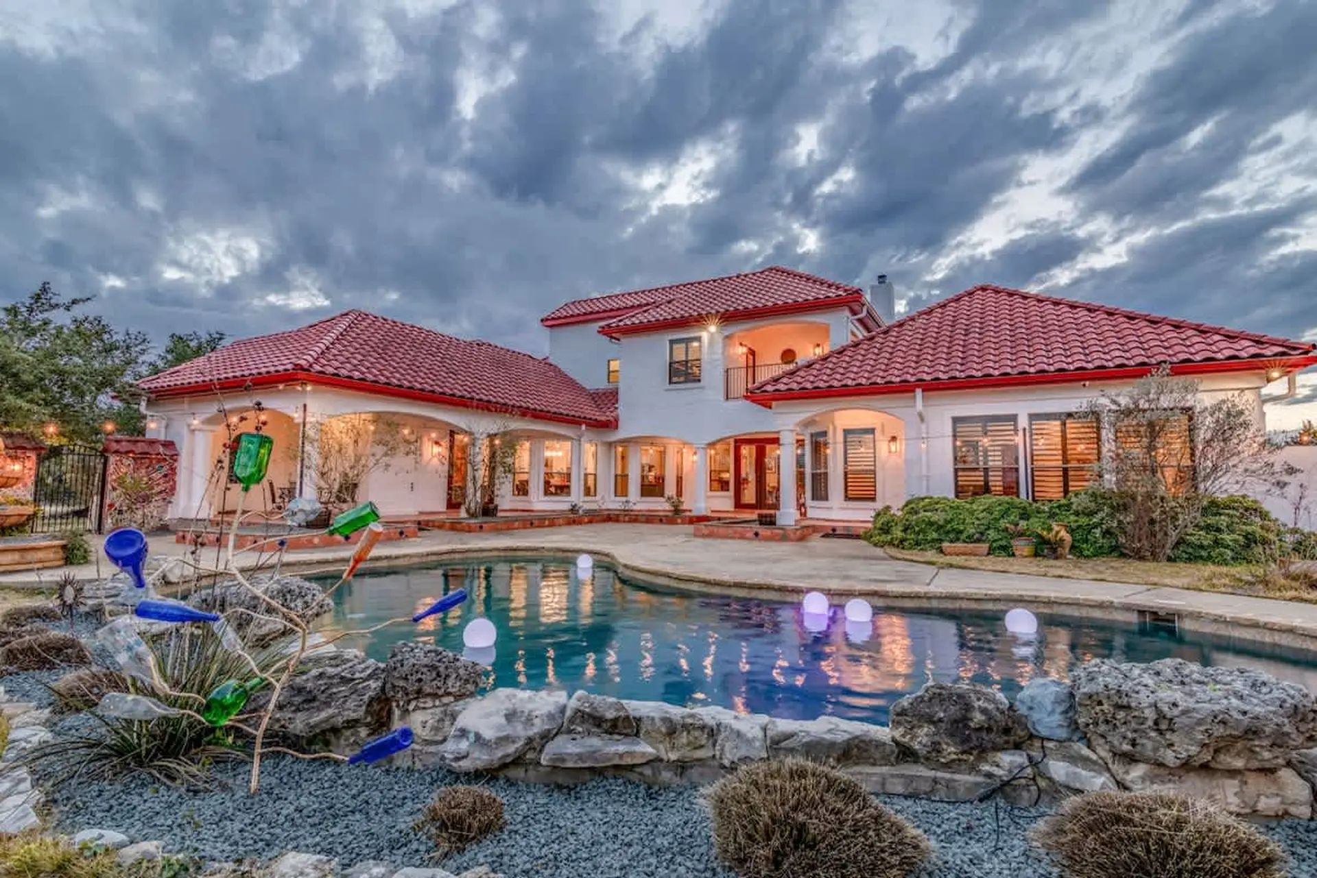 Luxury villa with red tile roof and swimming pool at dusk.