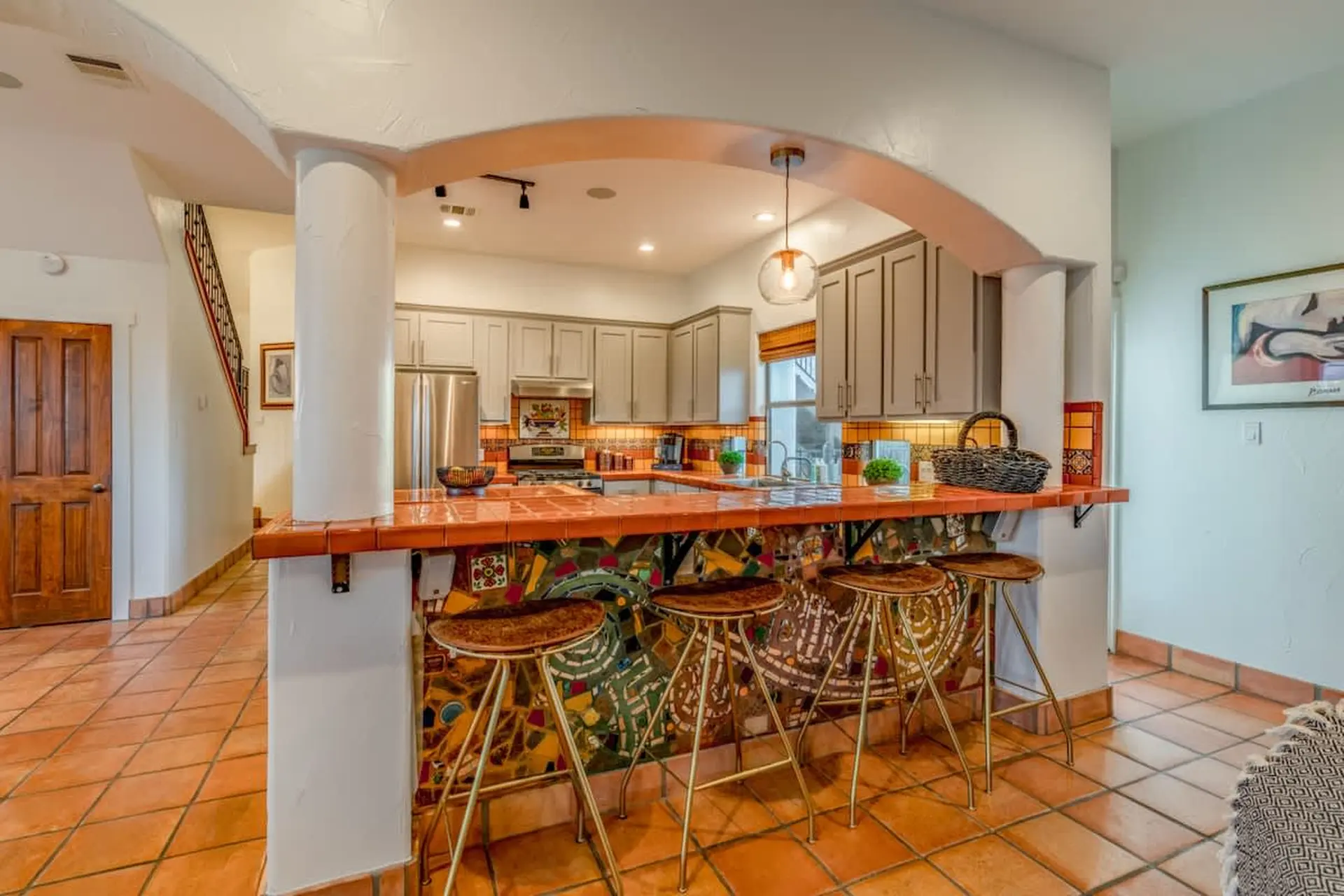 A kitchen with a tiled breakfast bar, stools, and cabinetry.