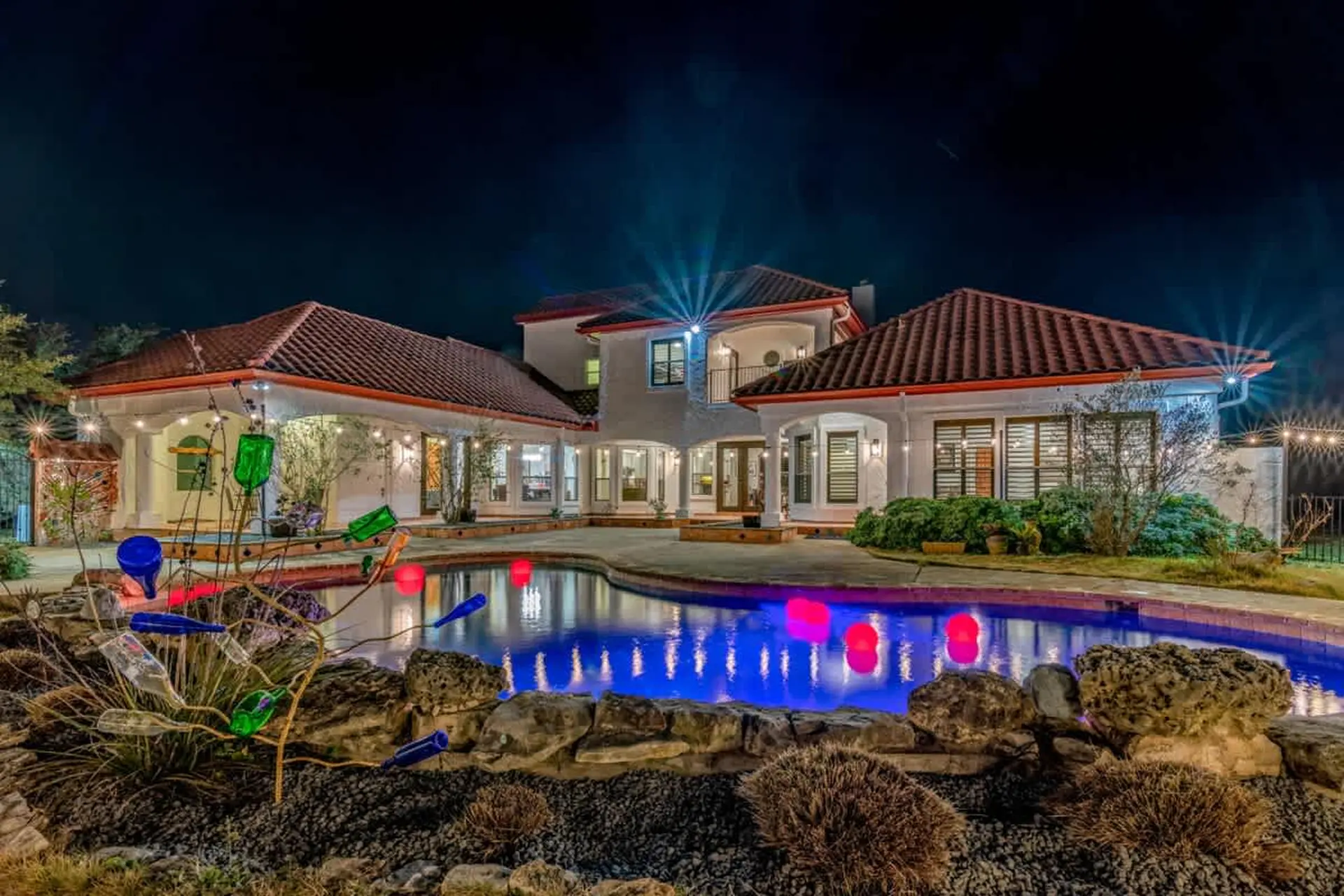 A modern mansion with a pool and outdoor lighting at night.