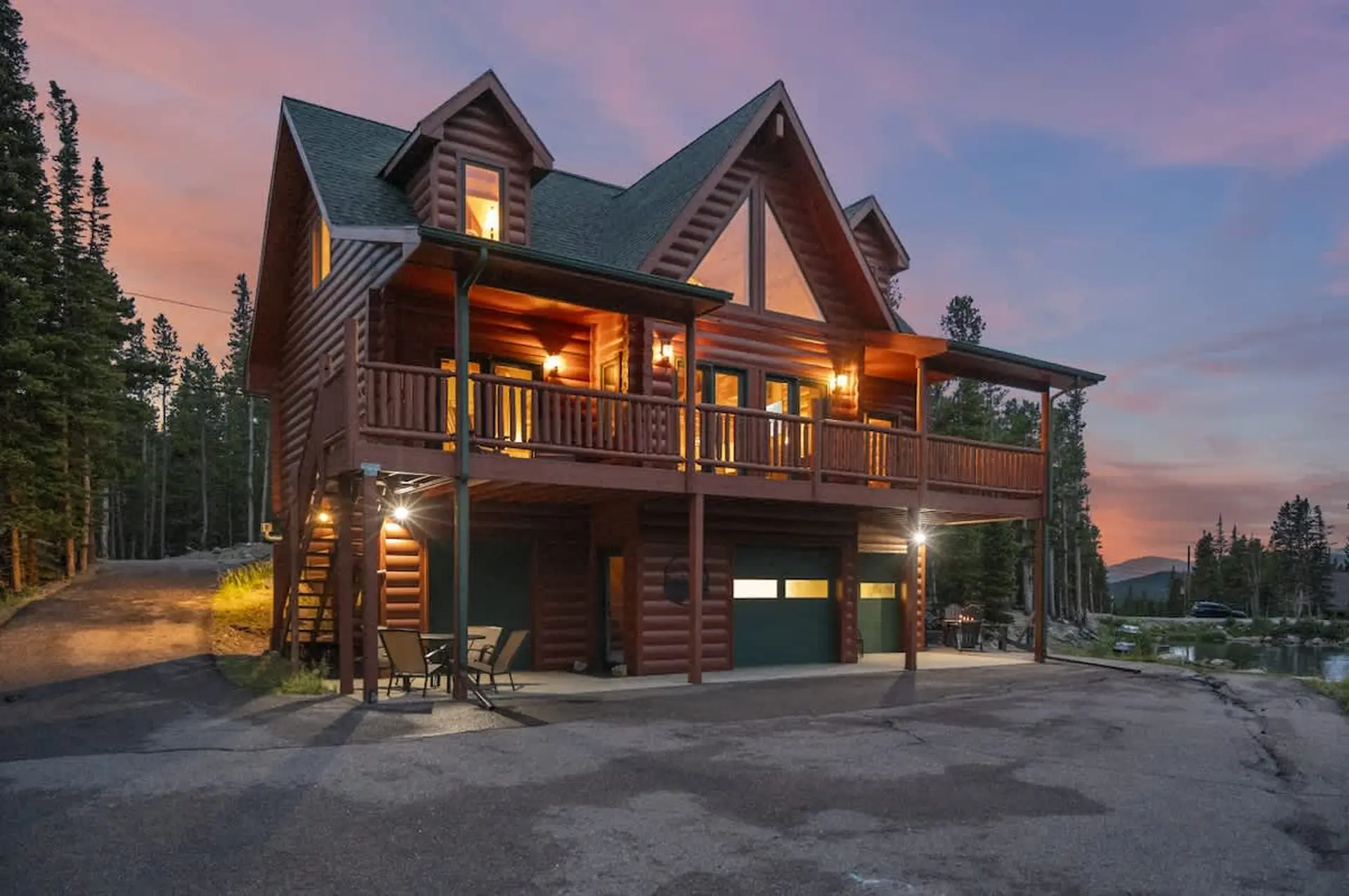 Luxury log cabin with a wraparound porch and mountain views at sunset.