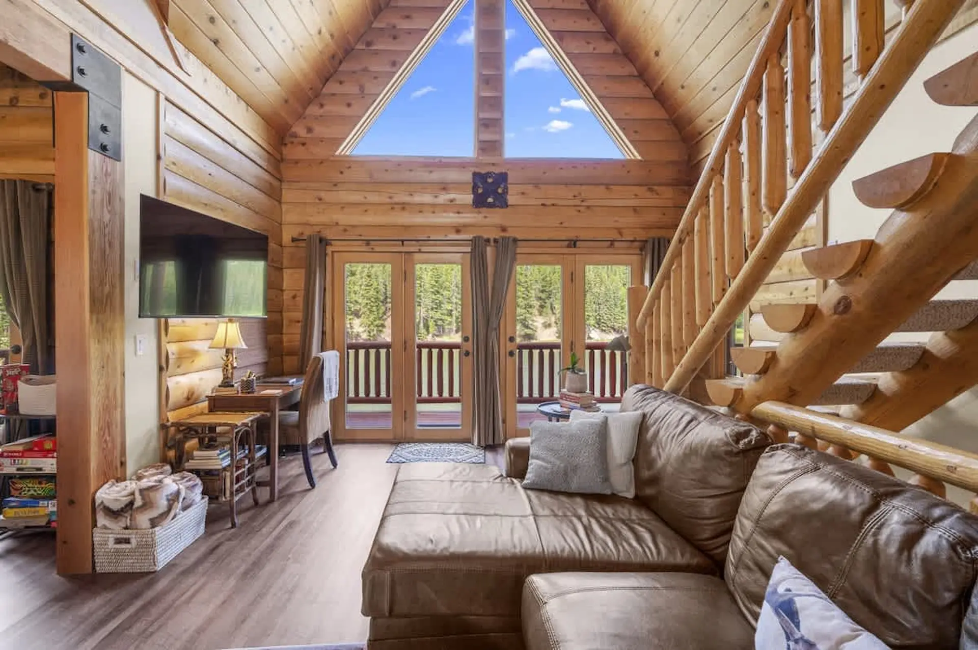A cozy living room with a leather sectional and a view of a forest through large windows.