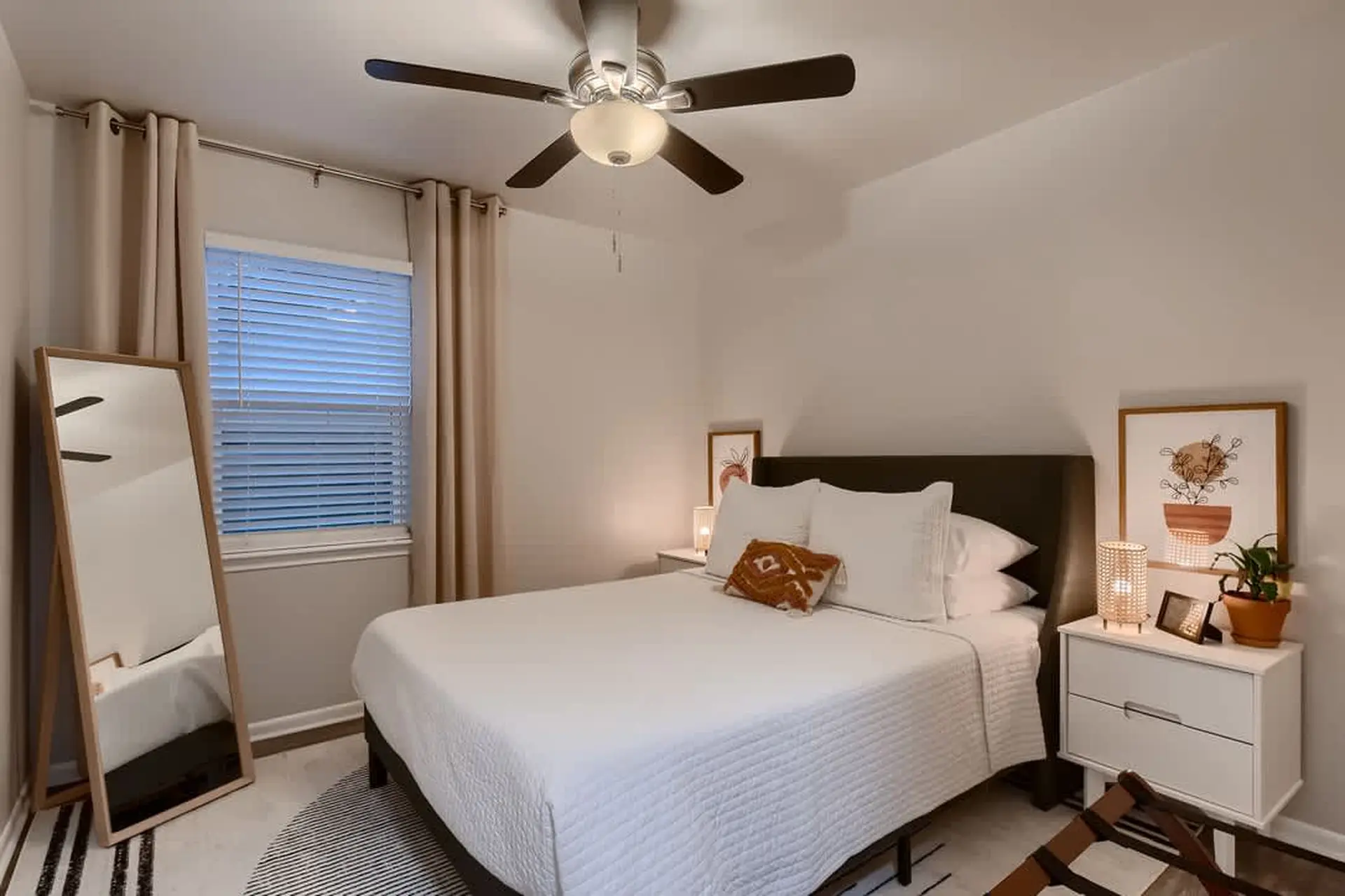 Bedroom with a bed, mirror, ceiling fan, and window with blinds.