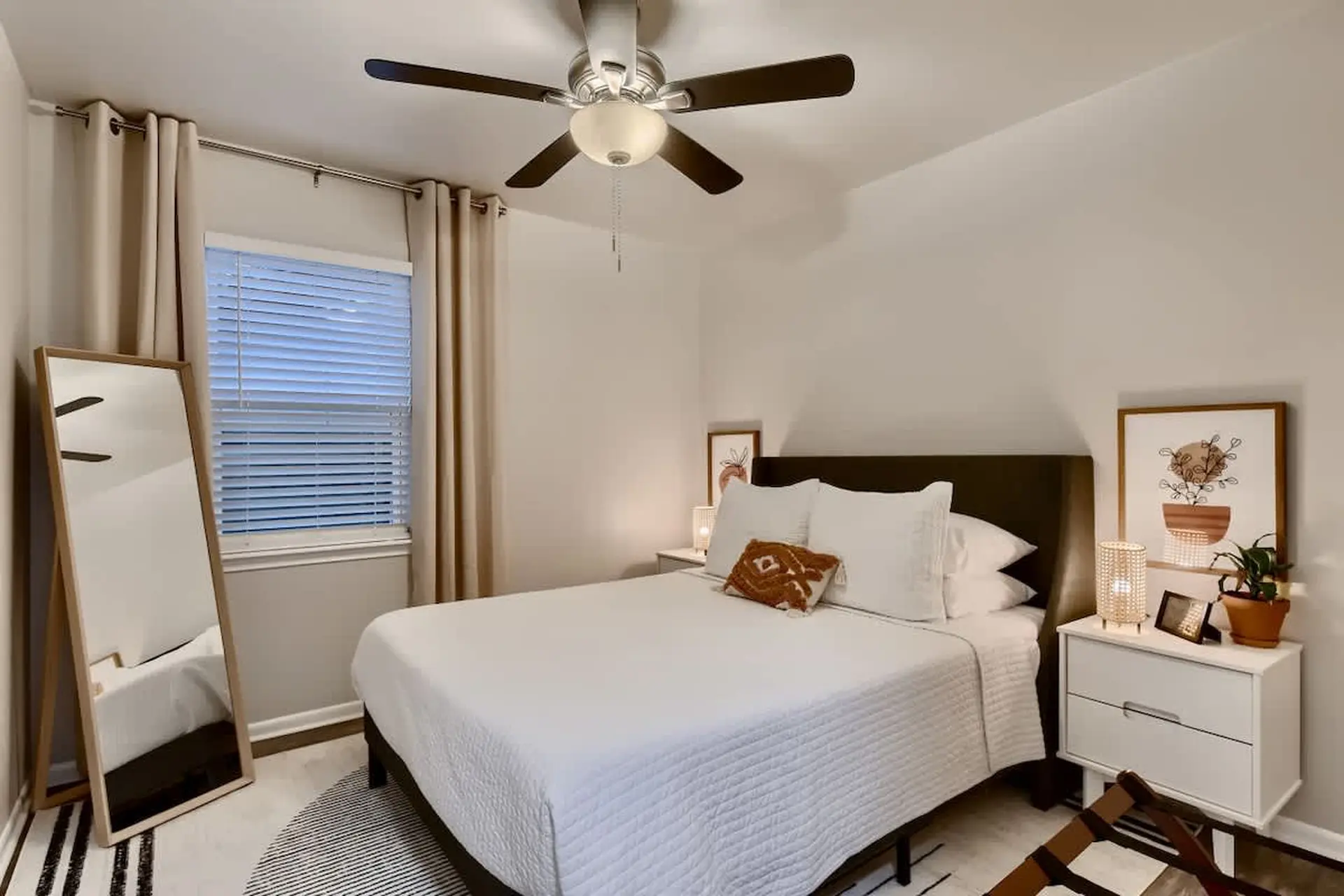 A bedroom with a bed, nightstand, mirror, and ceiling fan.