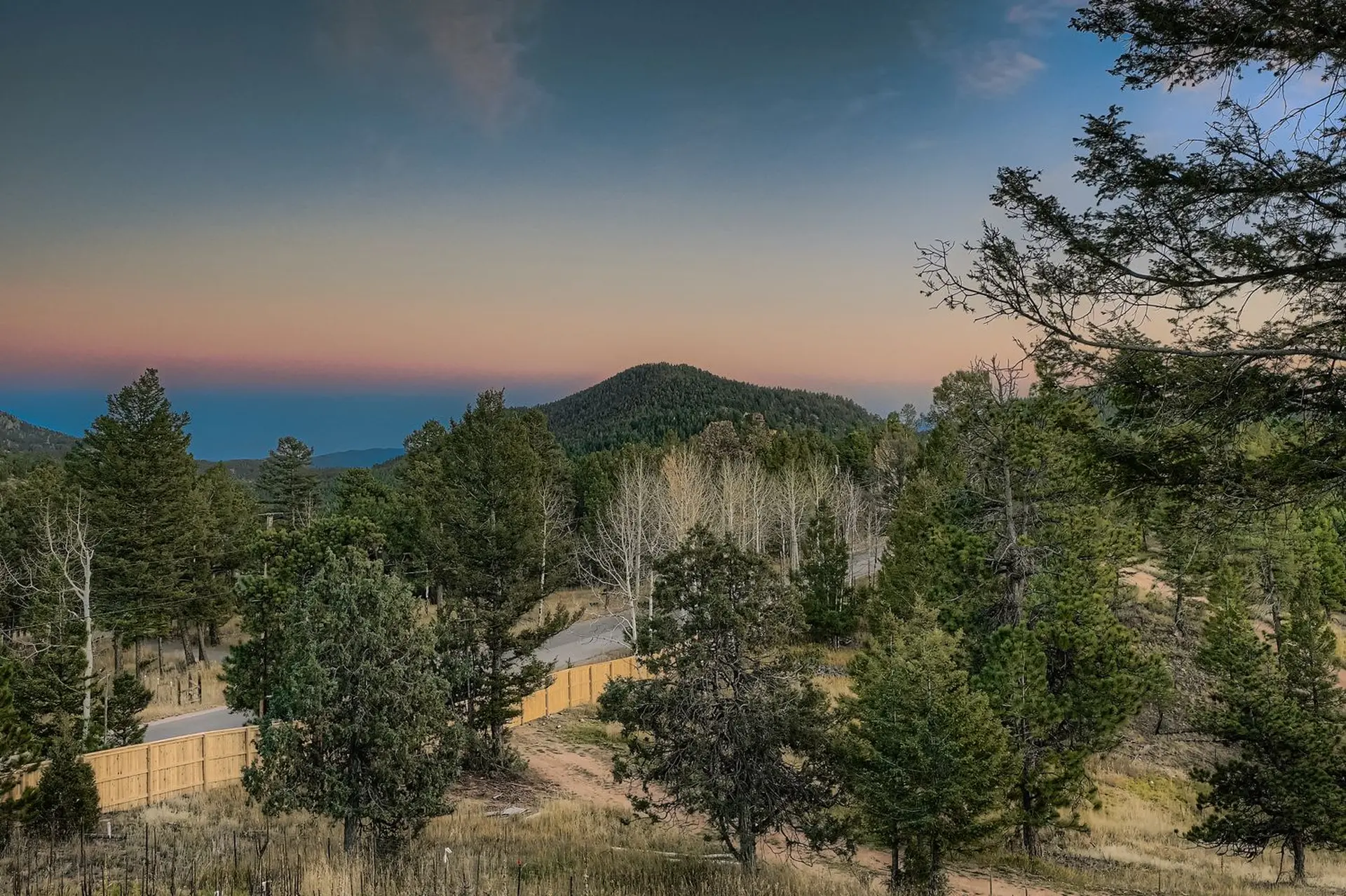 A twilight sky over a forest with a wooden fence and a mountain in the distance.
