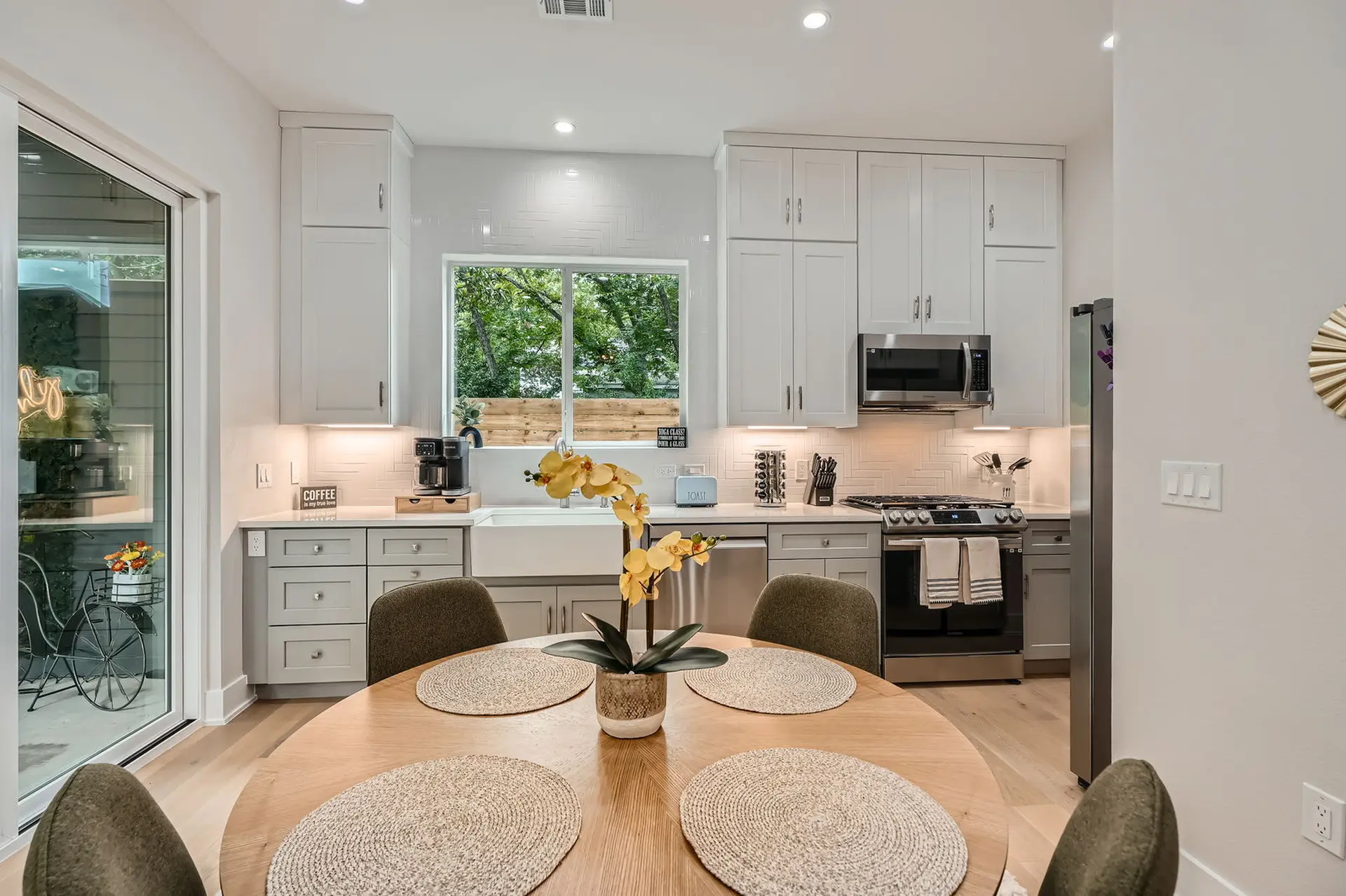 A bright, modern kitchen features white cabinets, a large sink, and a round dining table.