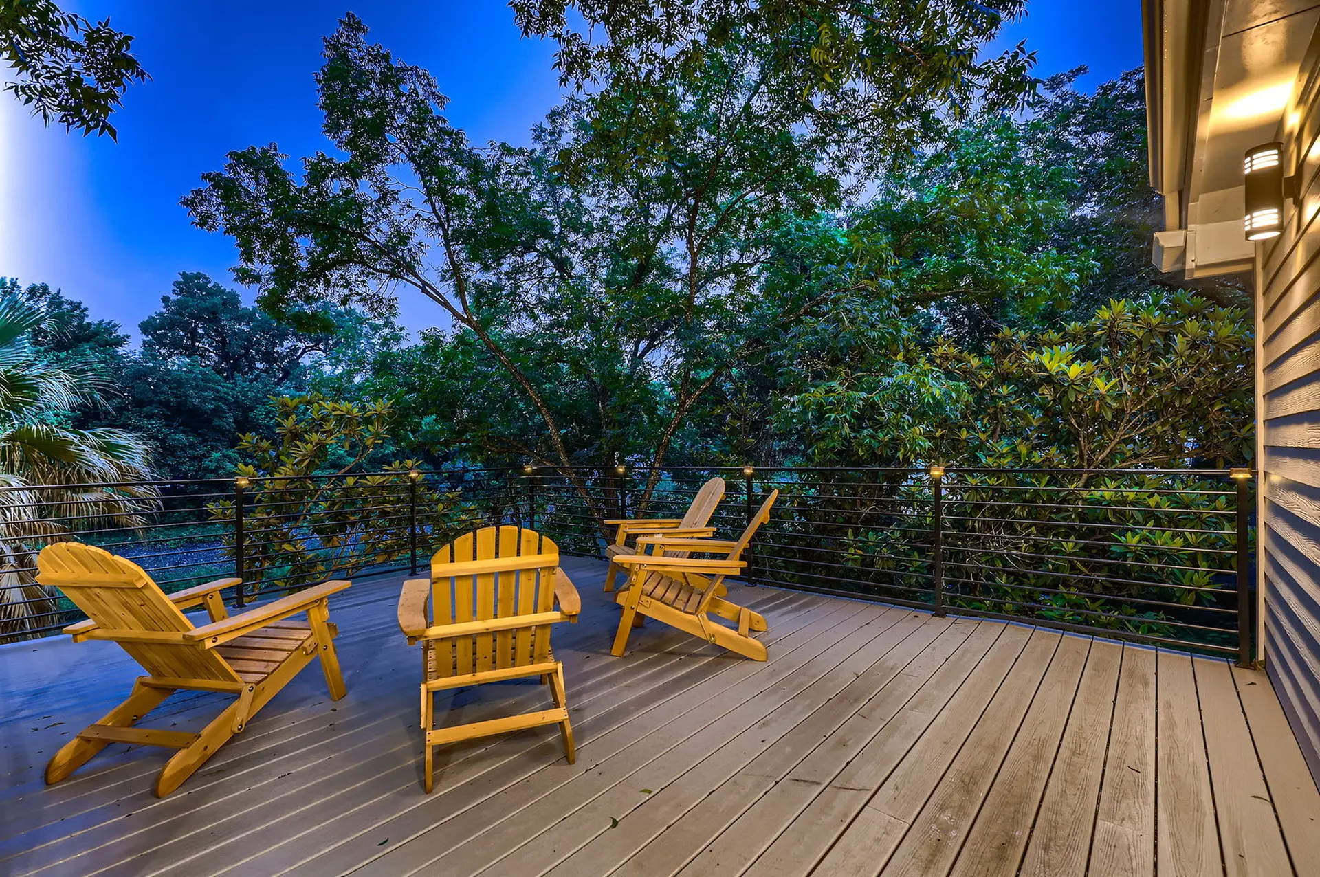 Wooden deck with chairs overlooking a lush forest at dusk.
