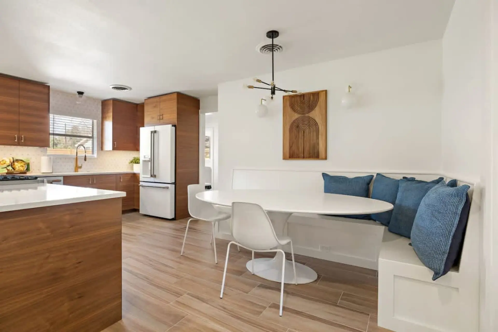 A modern kitchen with a white tulip table, banquette seating, and wood cabinets.
