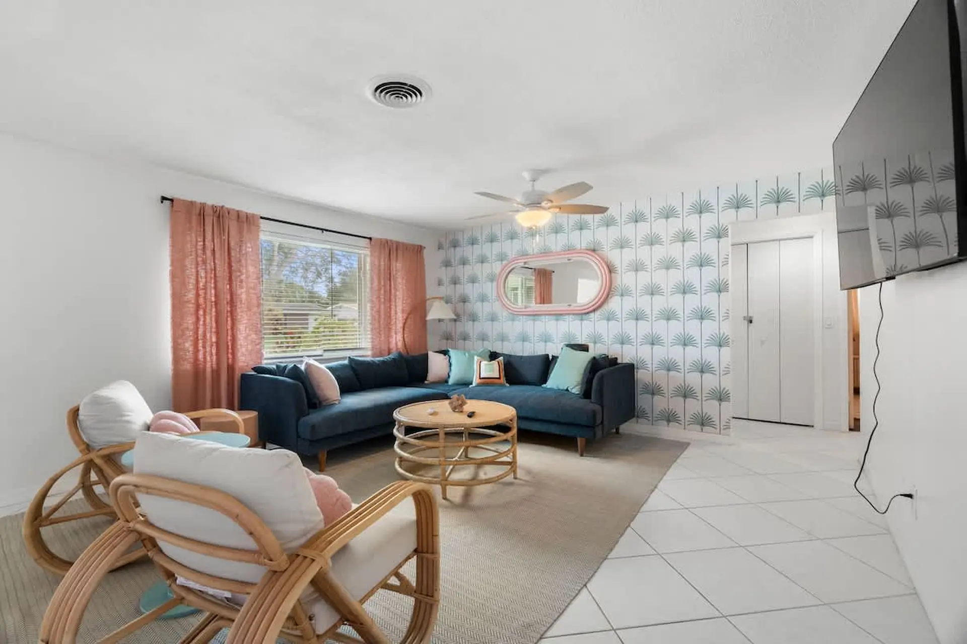 A living room with a blue sectional sofa, rattan chairs, a round coffee table, and tropical wallpape