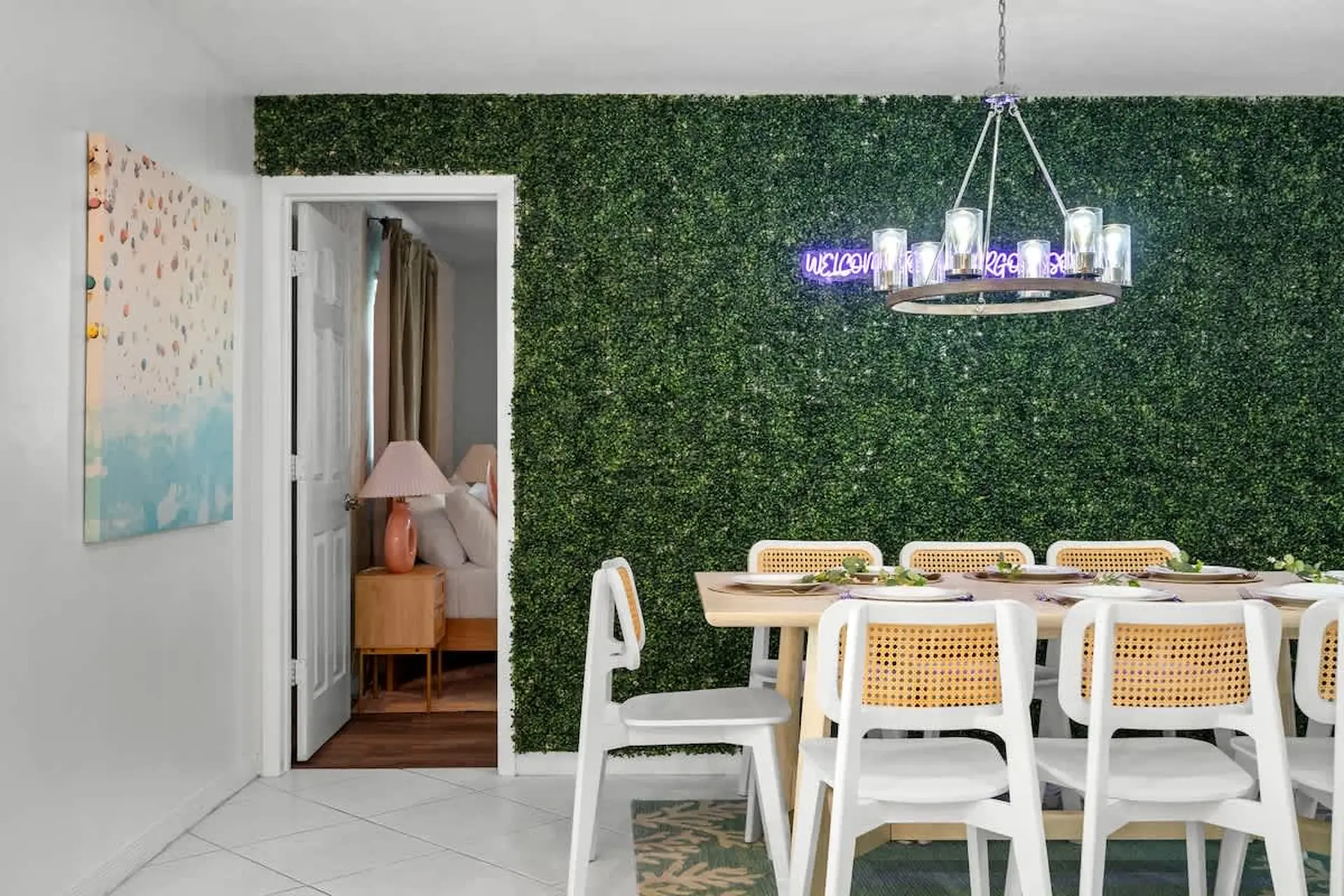 A dining room with a bright green, faux-grass wall and a chandelier.
