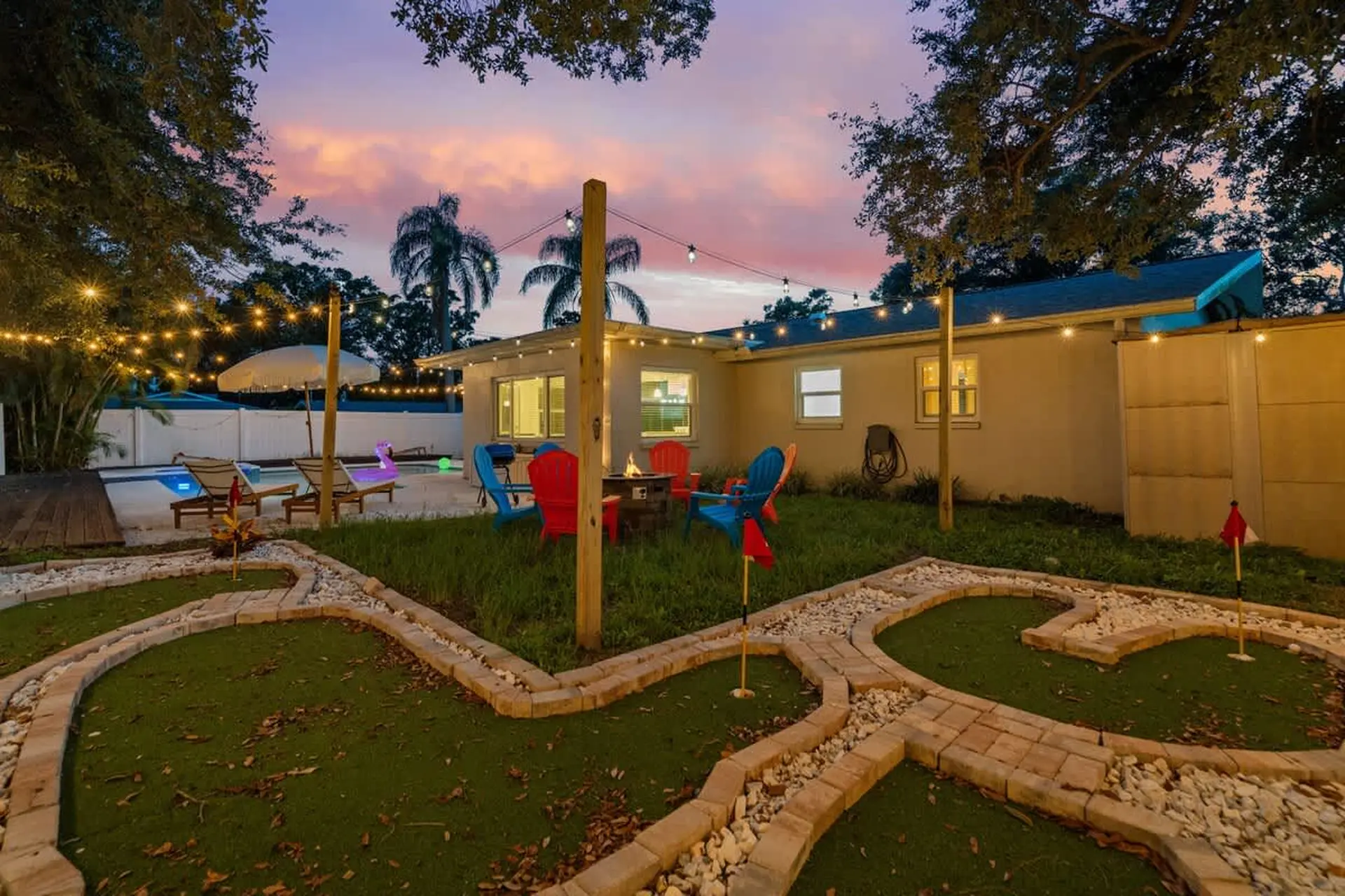 Backyard with mini golf, pool, fire pit, and string lights at dusk.