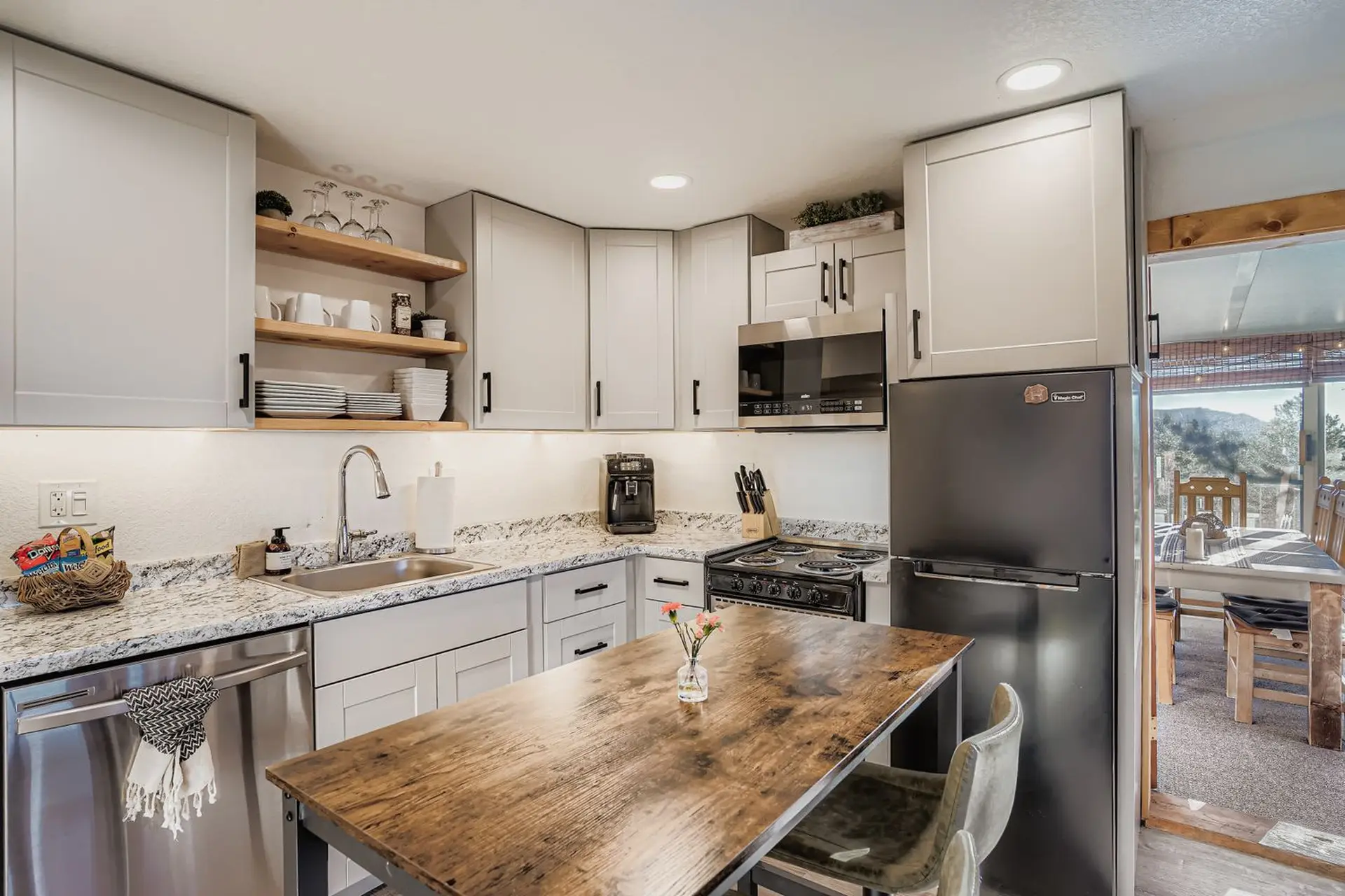 Kitchen with light grey cabinets, wooden table and chairs, and stainless steel appliances.