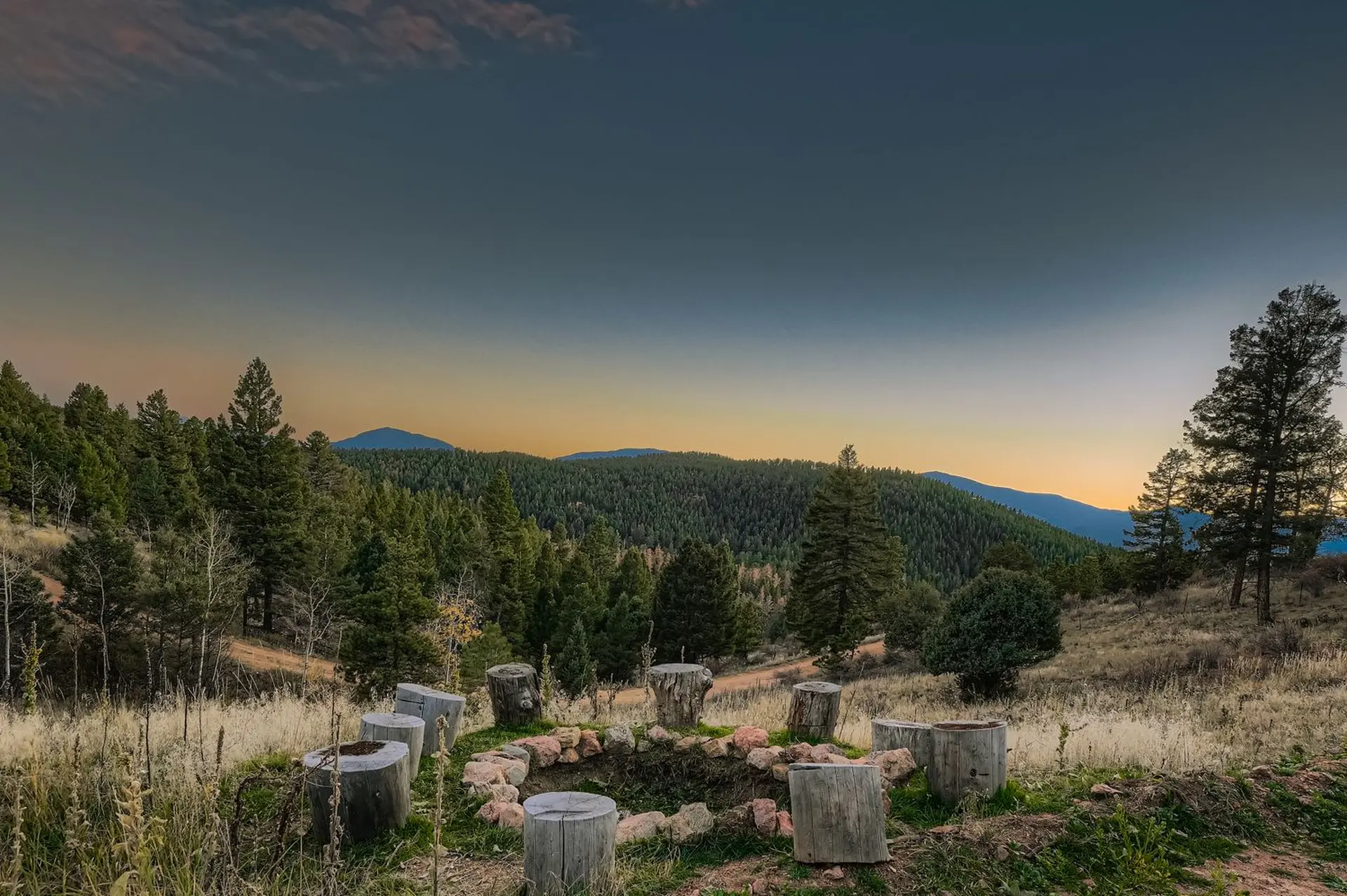 A fire pit area with log seats overlooks a forested valley at dusk.