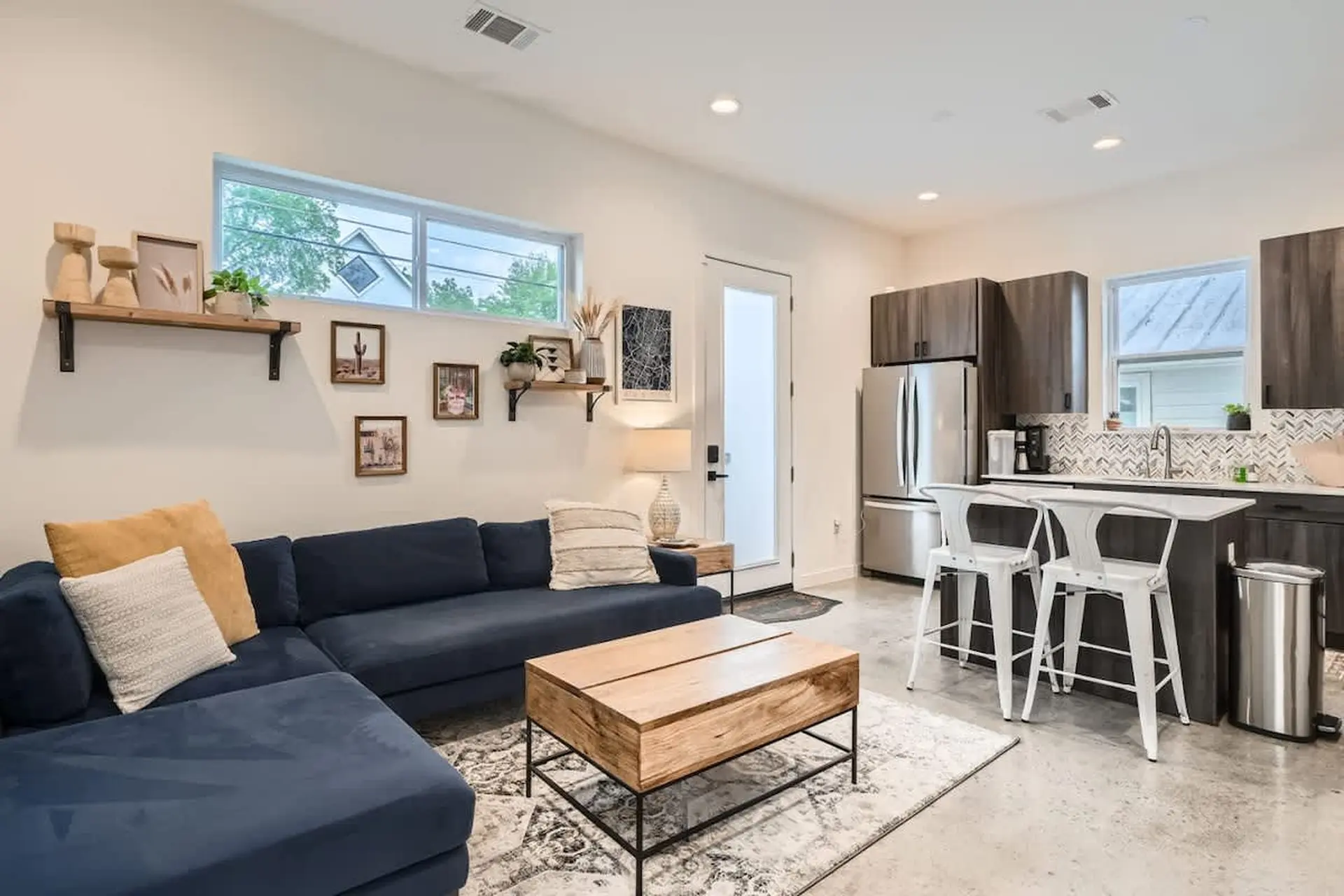 A modern living area with a blue sectional, coffee table, and kitchen island with bar stools.