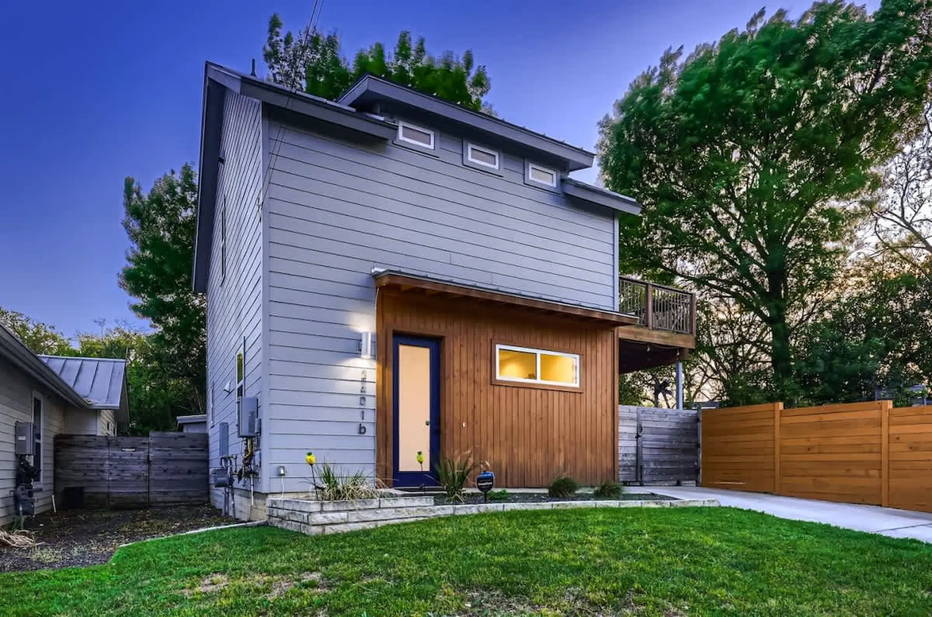 Modern gray and wood house with green lawn and wooden fence.