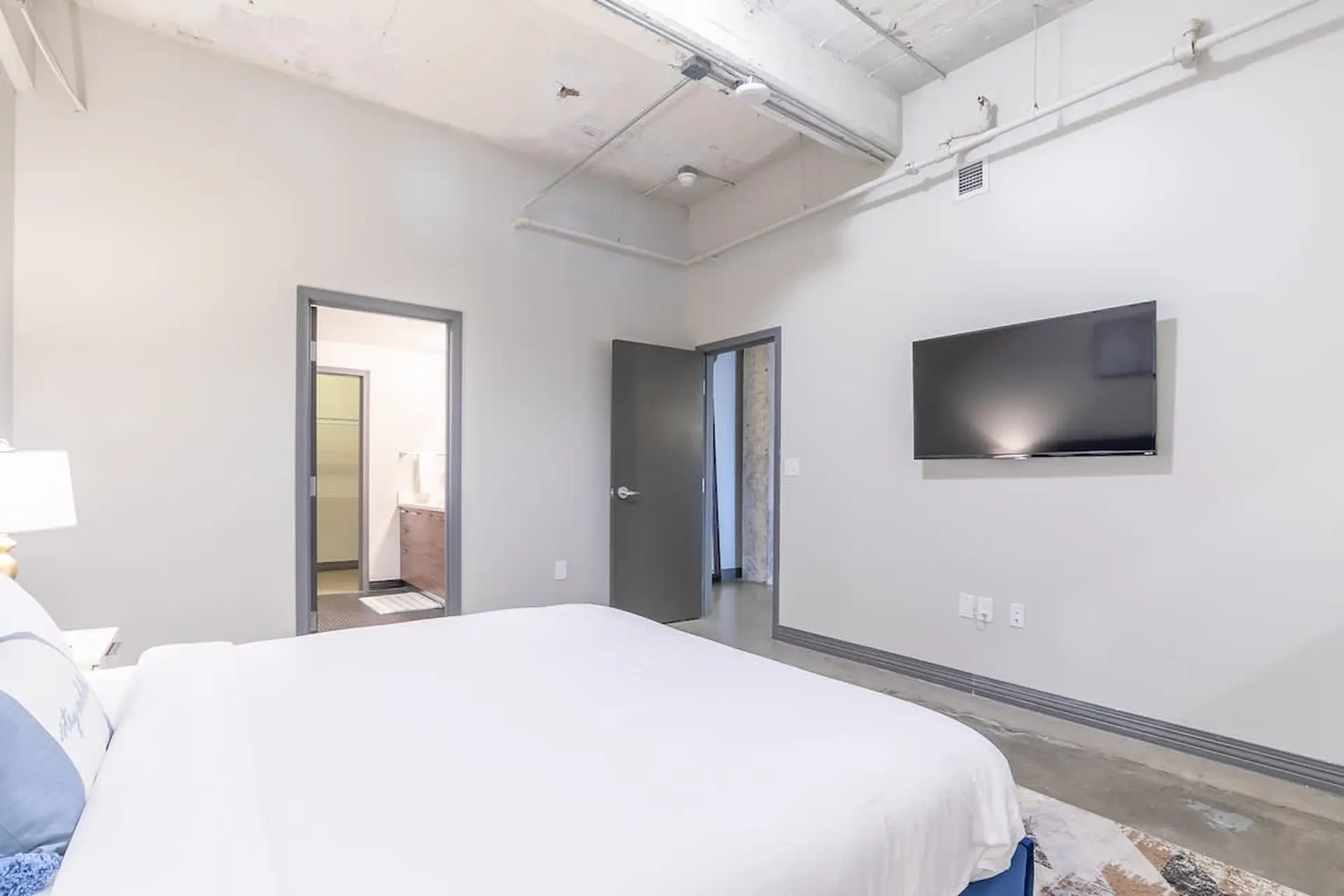 A bedroom with a bed, tv, and doors to other rooms.