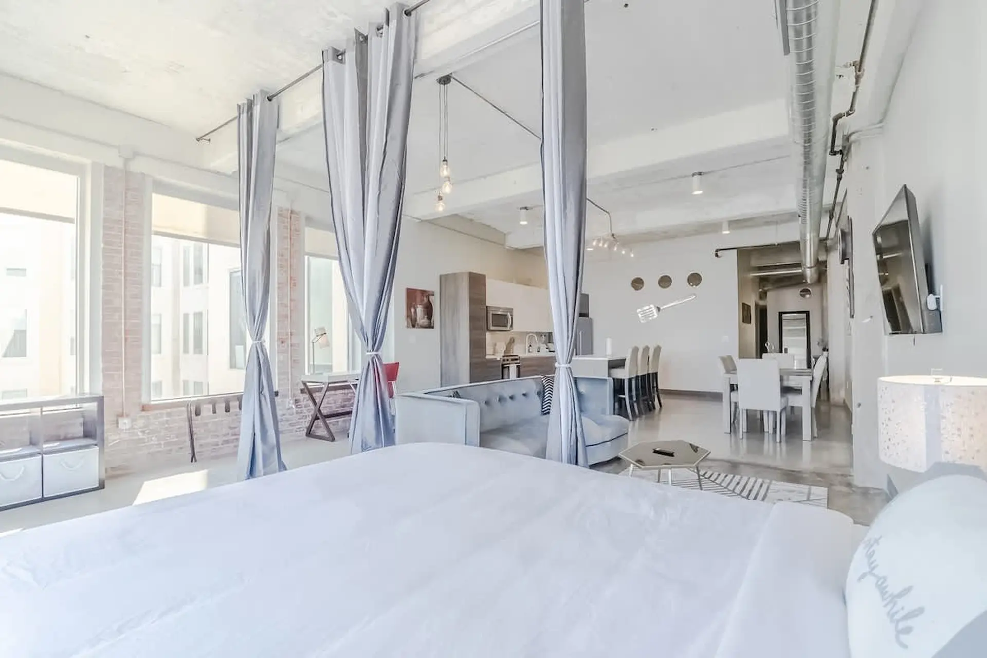 Modern studio apartment with bed, sofa, kitchen, dining area, and large windows.