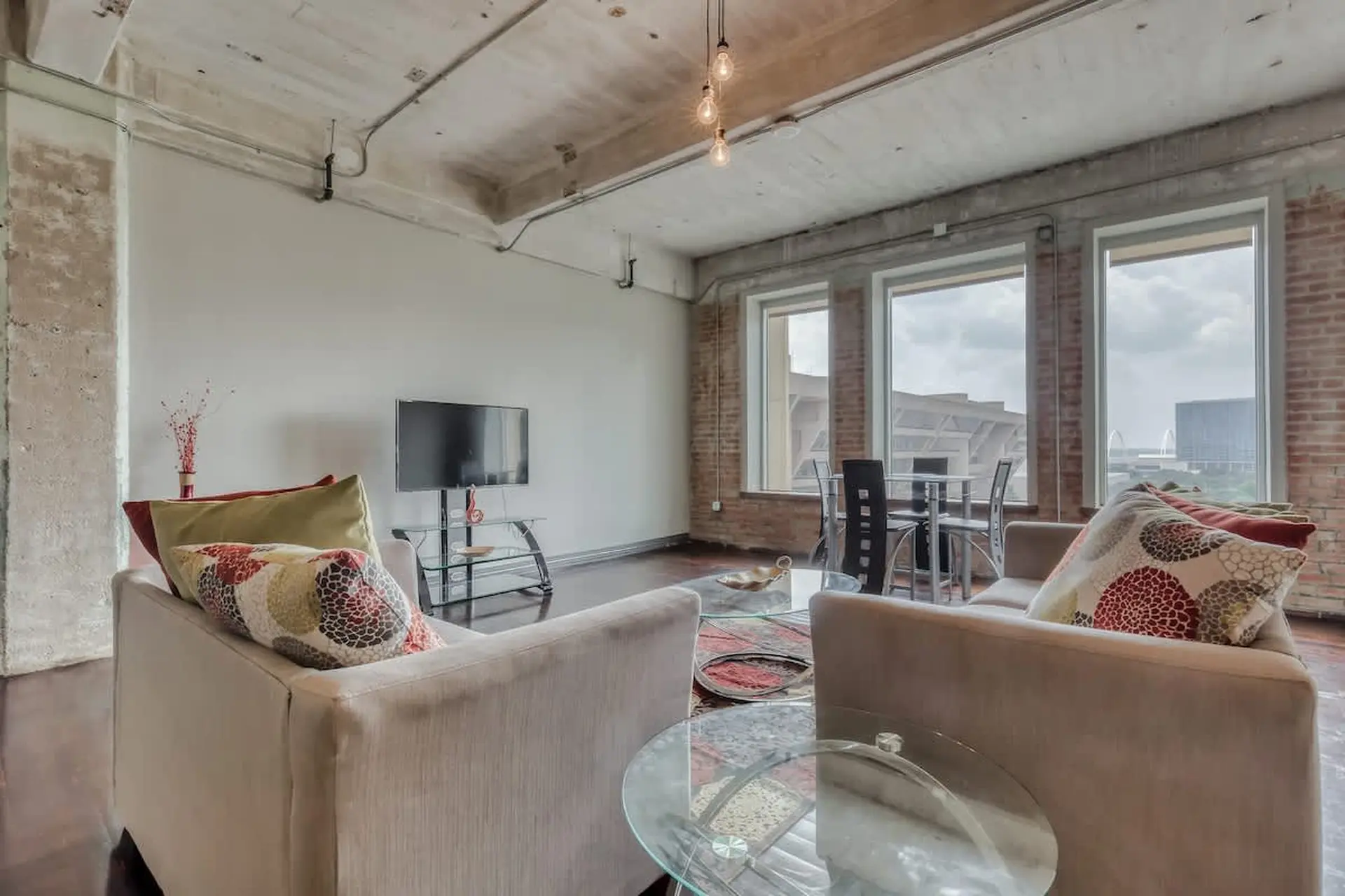 Living room with sofas, coffee table, and TV. Large windows overlook a city skyline.