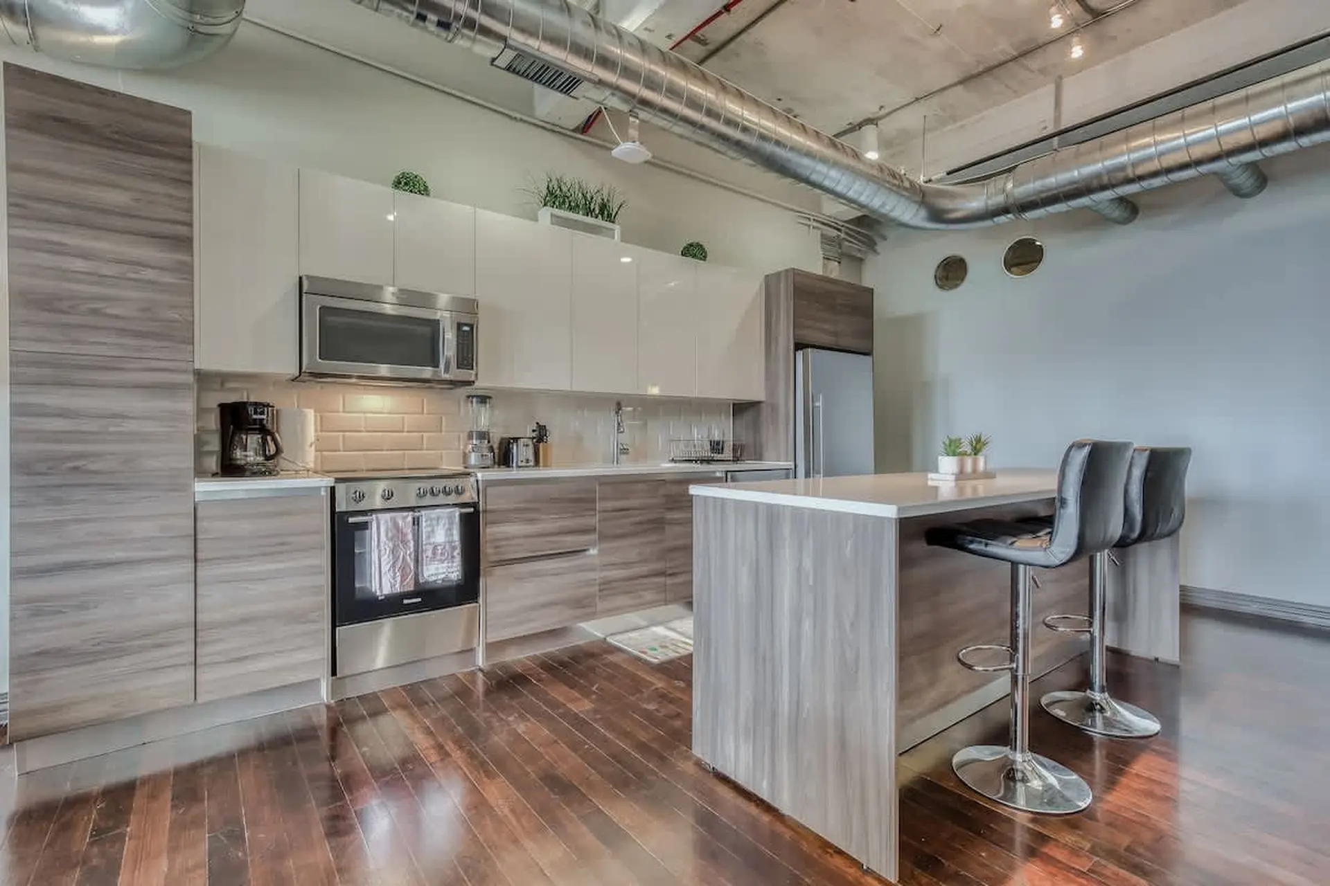 A modern kitchen with stainless steel appliances, wood cabinetry, and a kitchen island with bar stoo