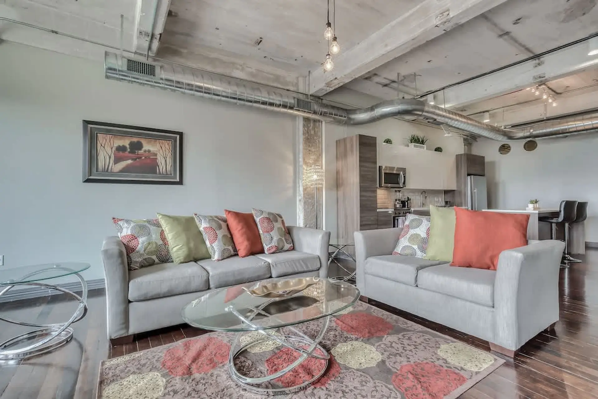 Loft living room with exposed ductwork, sofas, coffee table, and kitchen area.