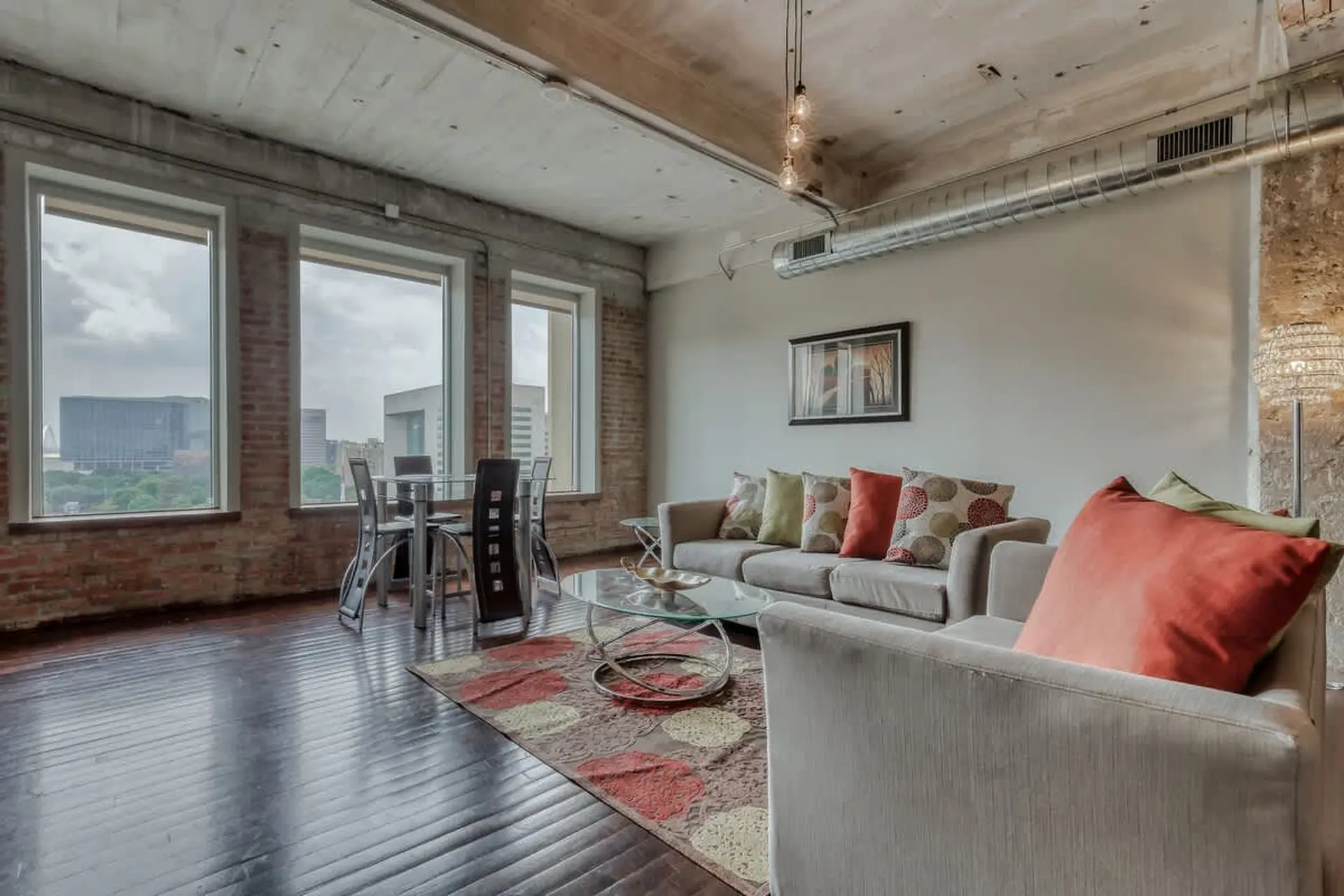 Living room with exposed brick, large windows, and a sofa with colorful pillows.
