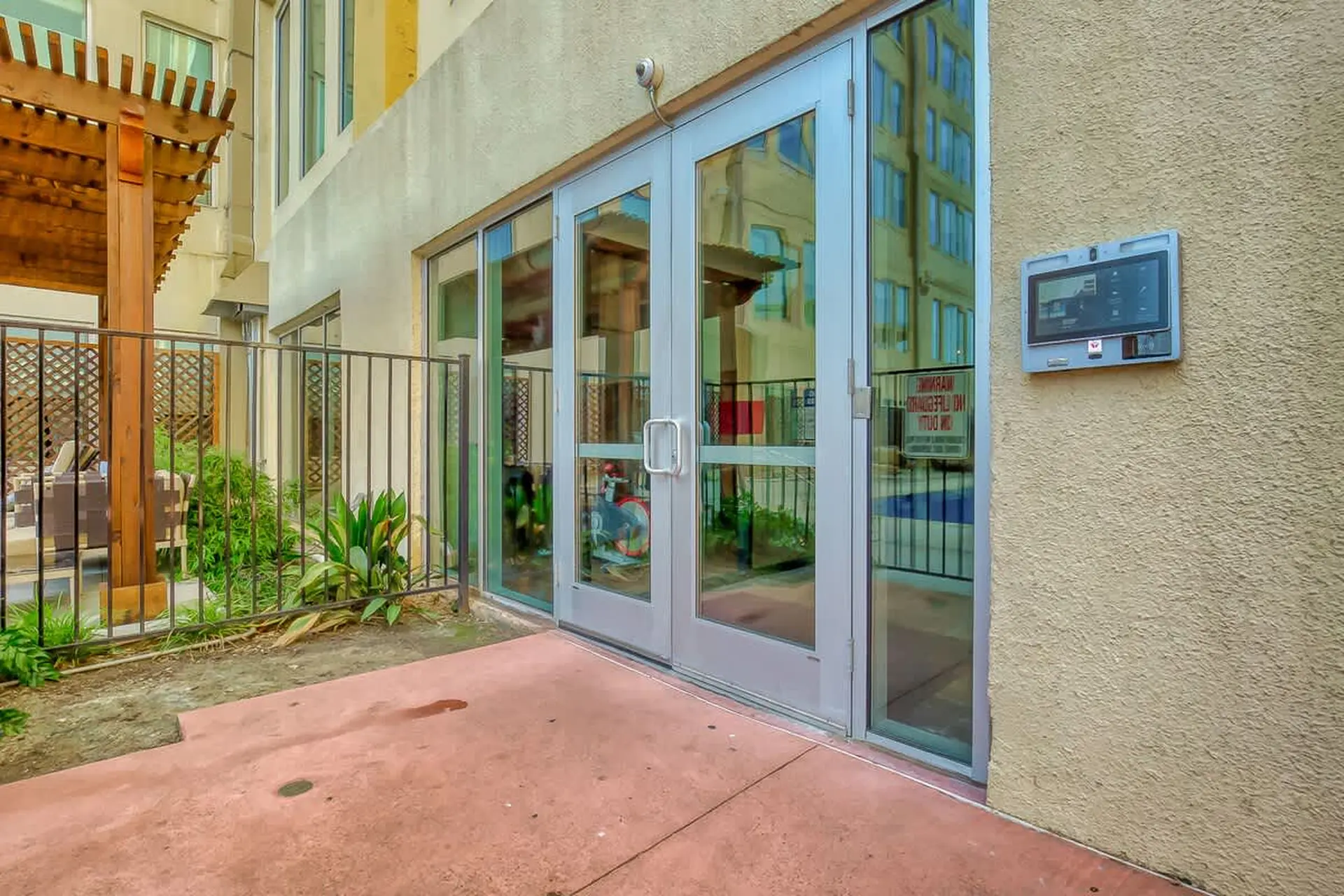 Glass doors with metal frames, surrounded by plants and a security camera.