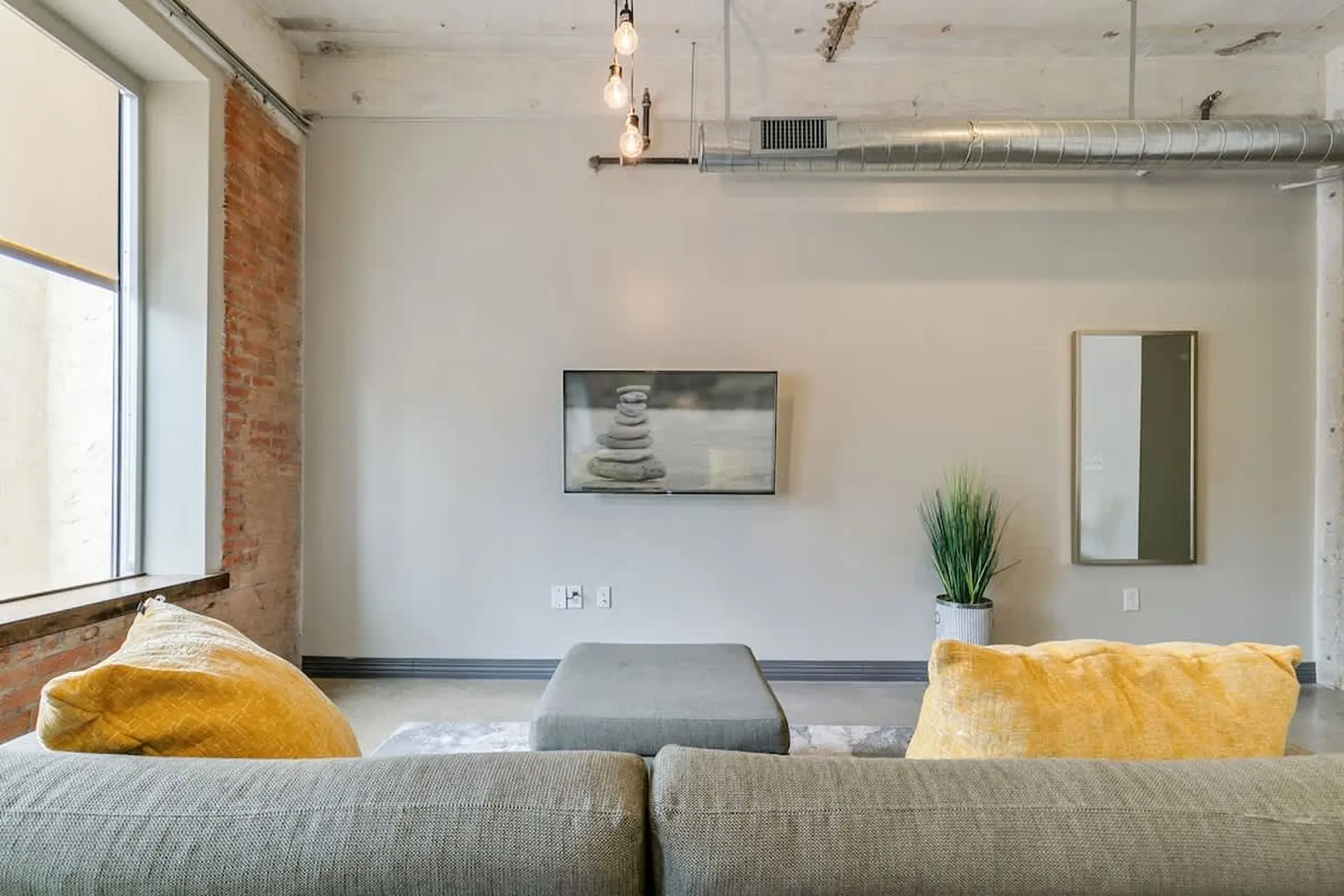 Living room with a gray couch, yellow pillows, ottoman, and mounted tv.