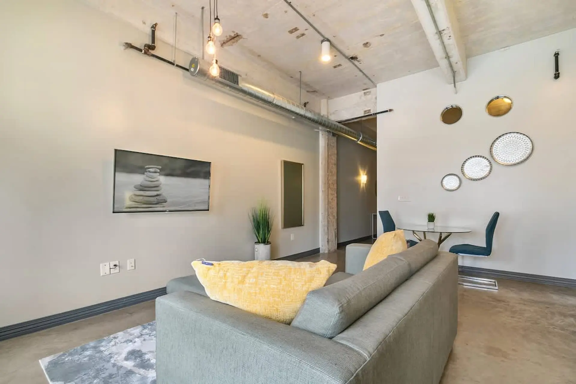 Modern living room with a grey couch, yellow pillows, and a glass dining table.