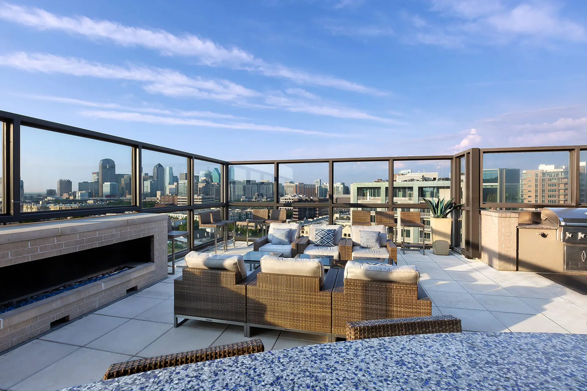 A rooftop patio with a fireplace, grill, and seating overlooking a city skyline.