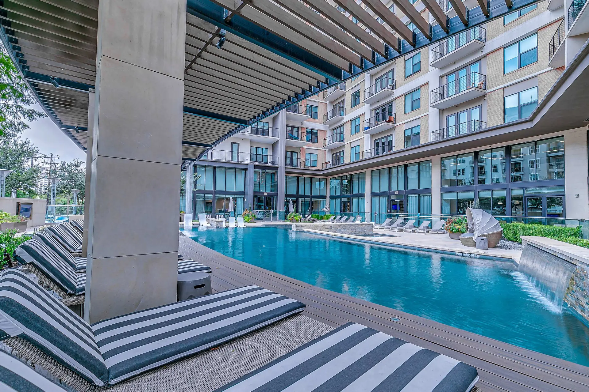 A modern apartment building with a swimming pool, lounge chairs, and waterfalls.