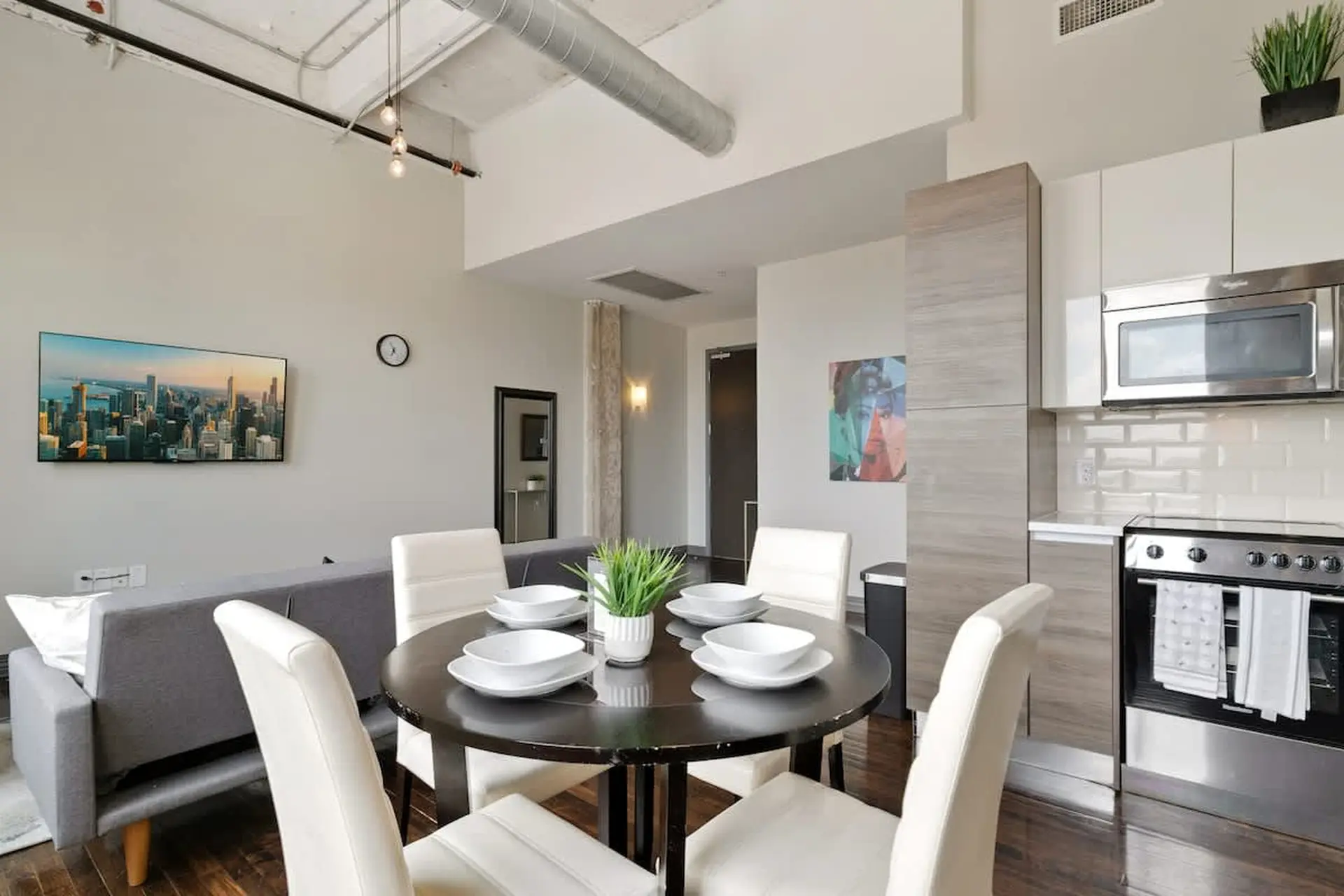 A dining table with place settings sits in front of a sofa, with a modern kitchen in the background.