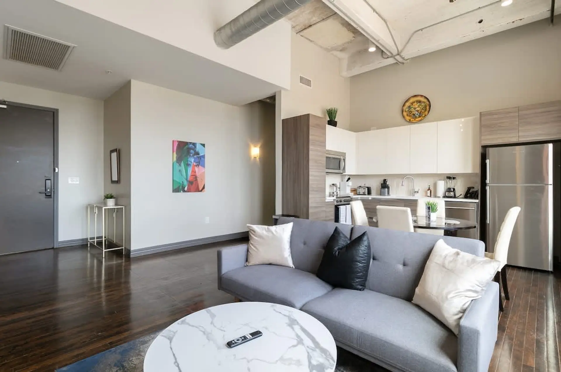 Modern loft living room with gray sofa, white marble coffee table, and sleek kitchen.