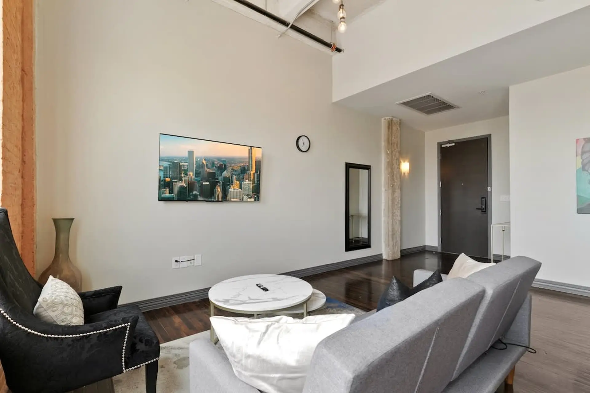 Modern living room with city view TV, black accent chair, and gray sofa.