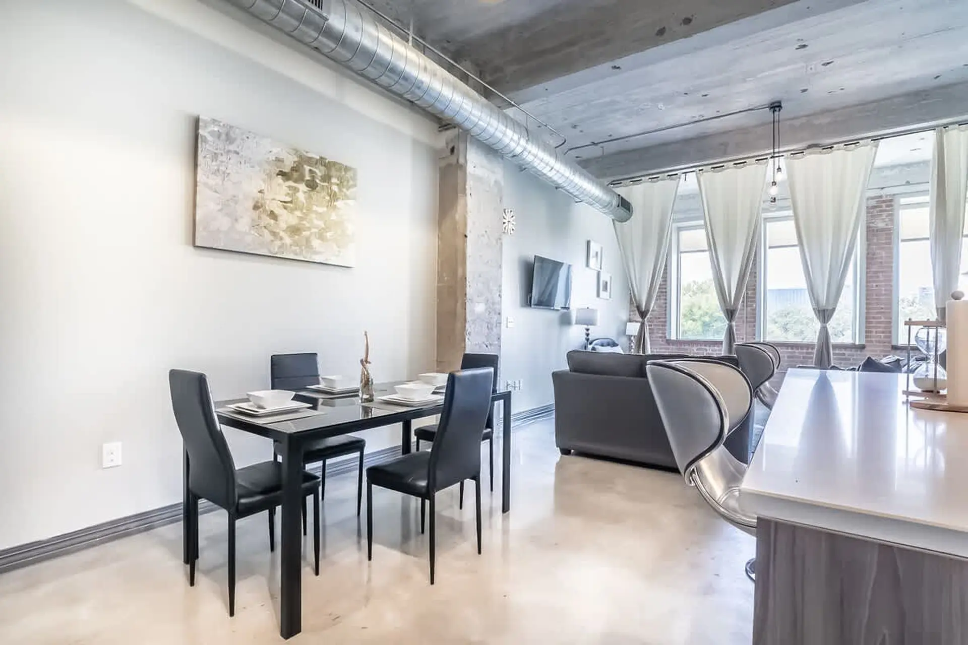 Modern dining area with abstract art and a living room with a sofa and large windows.