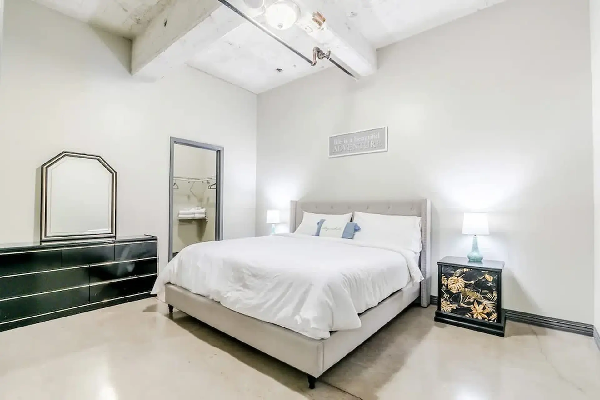 A well-lit bedroom with a king-sized bed, dresser, mirror, and nightstand.