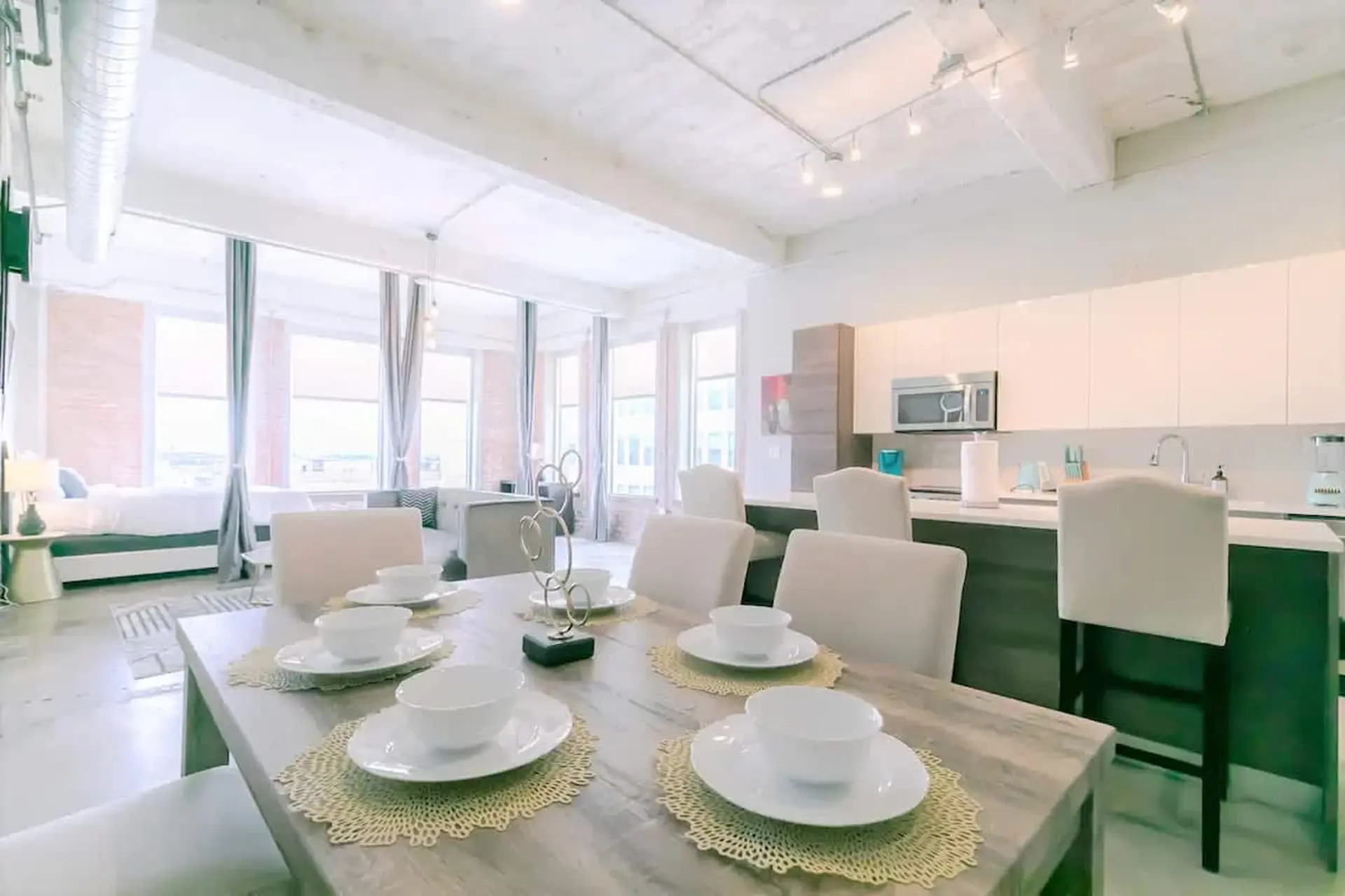 A dining table with place settings and chairs is in the foreground of a modern living space.