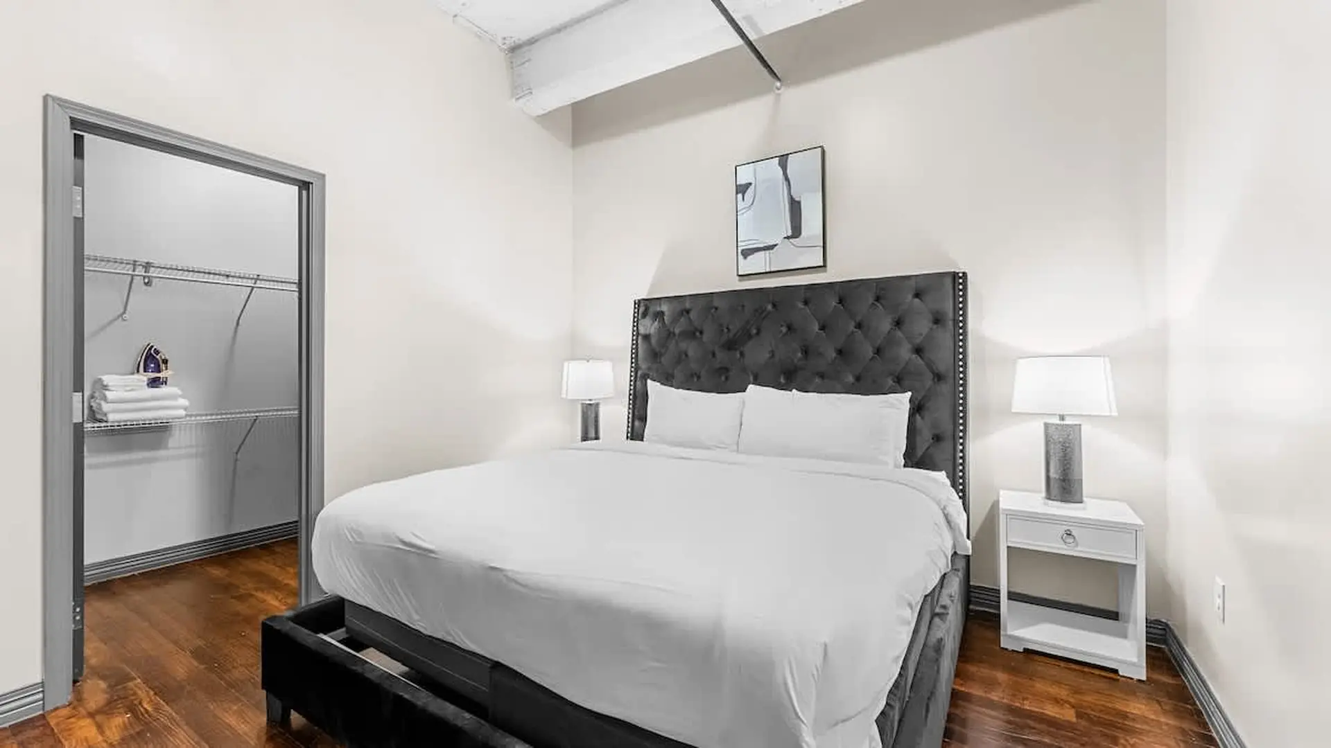 A master bedroom with a tufted headboard bed, white bedding, and a closet.