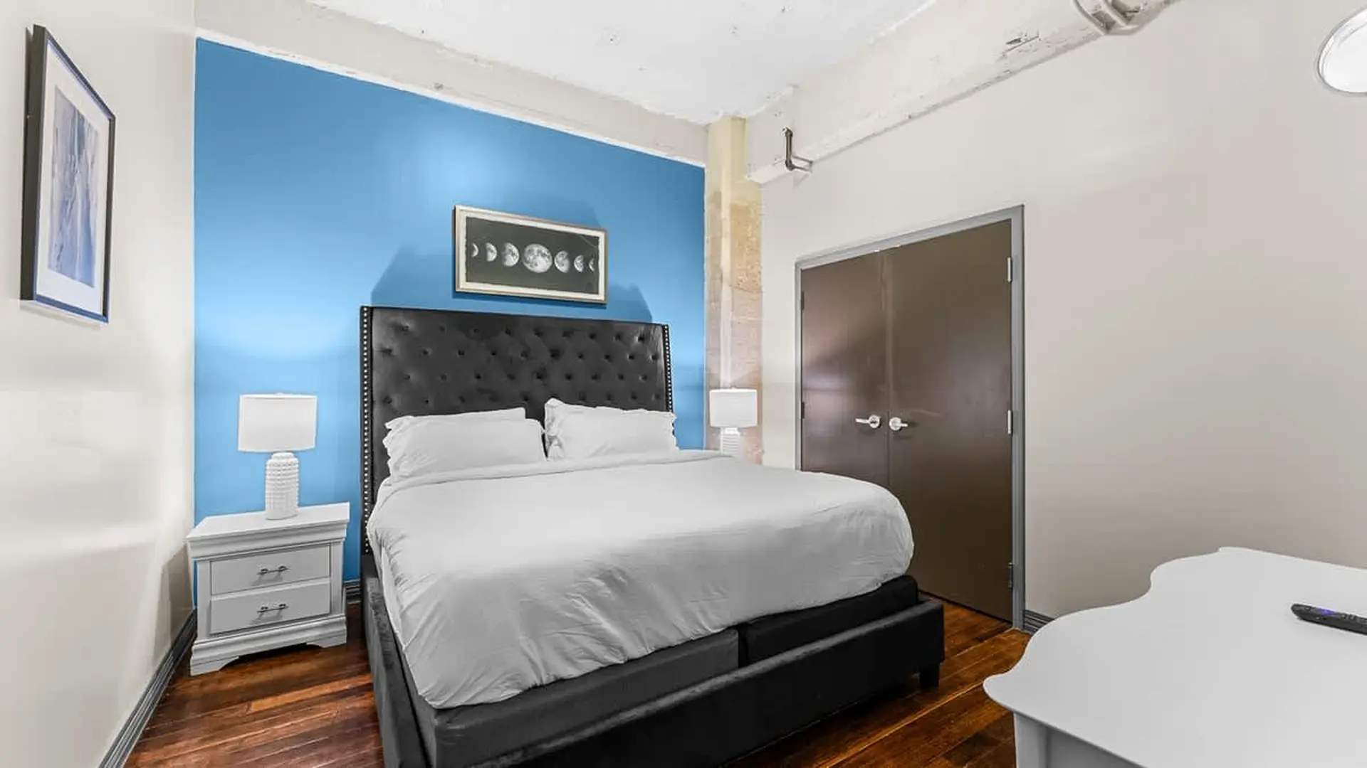 A bed with a black tufted headboard, white linens, and two white lamps on nightstands.