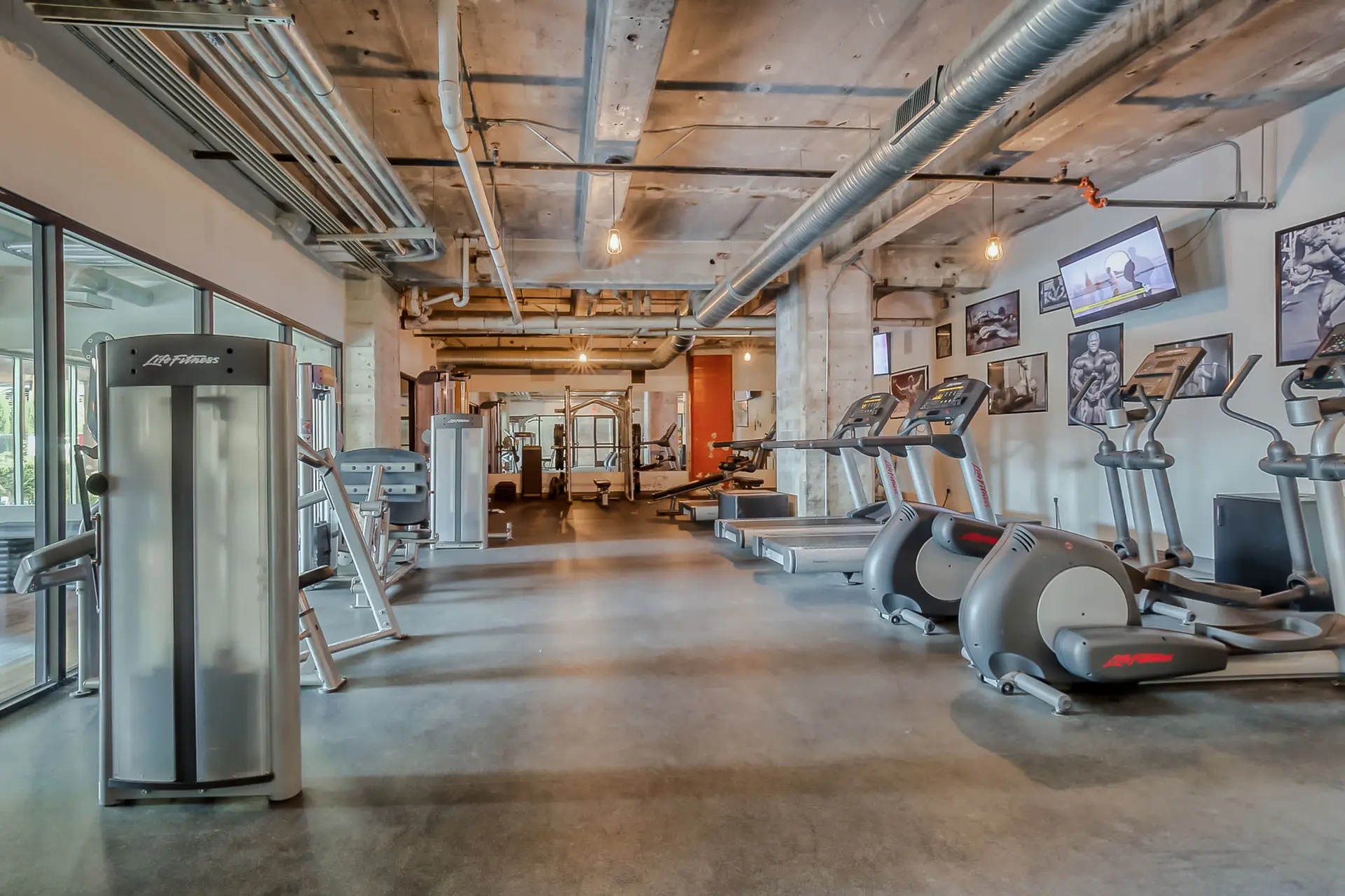 A gym with cardio machines, weight machines, and posters of bodybuilders.