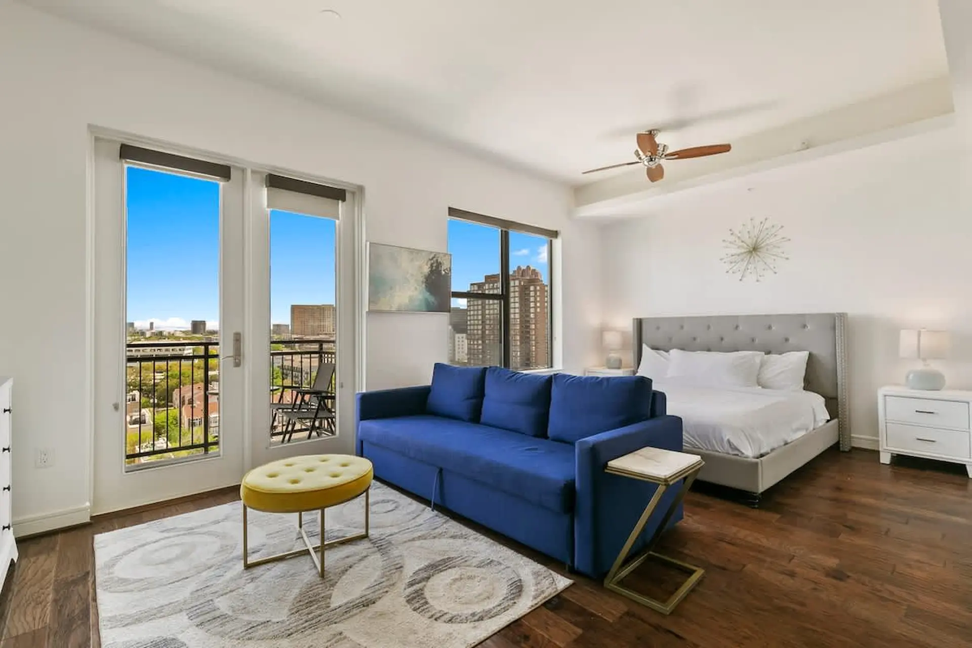 A bright studio apartment with a blue sofa, bed, and balcony view.