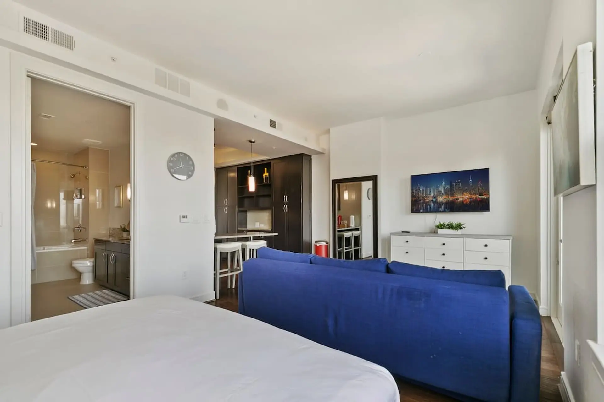 A spacious studio apartment with a bed, sofa, and kitchen area.