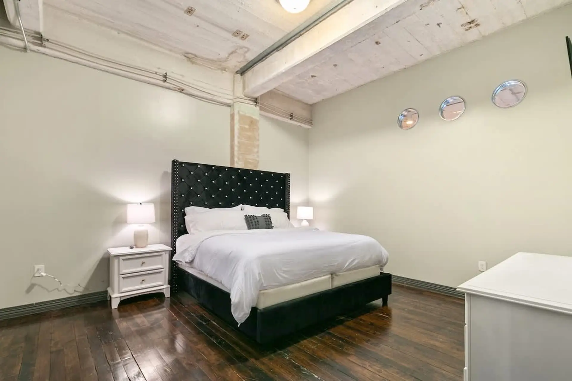 A bedroom with a black tufted headboard and white bedding.