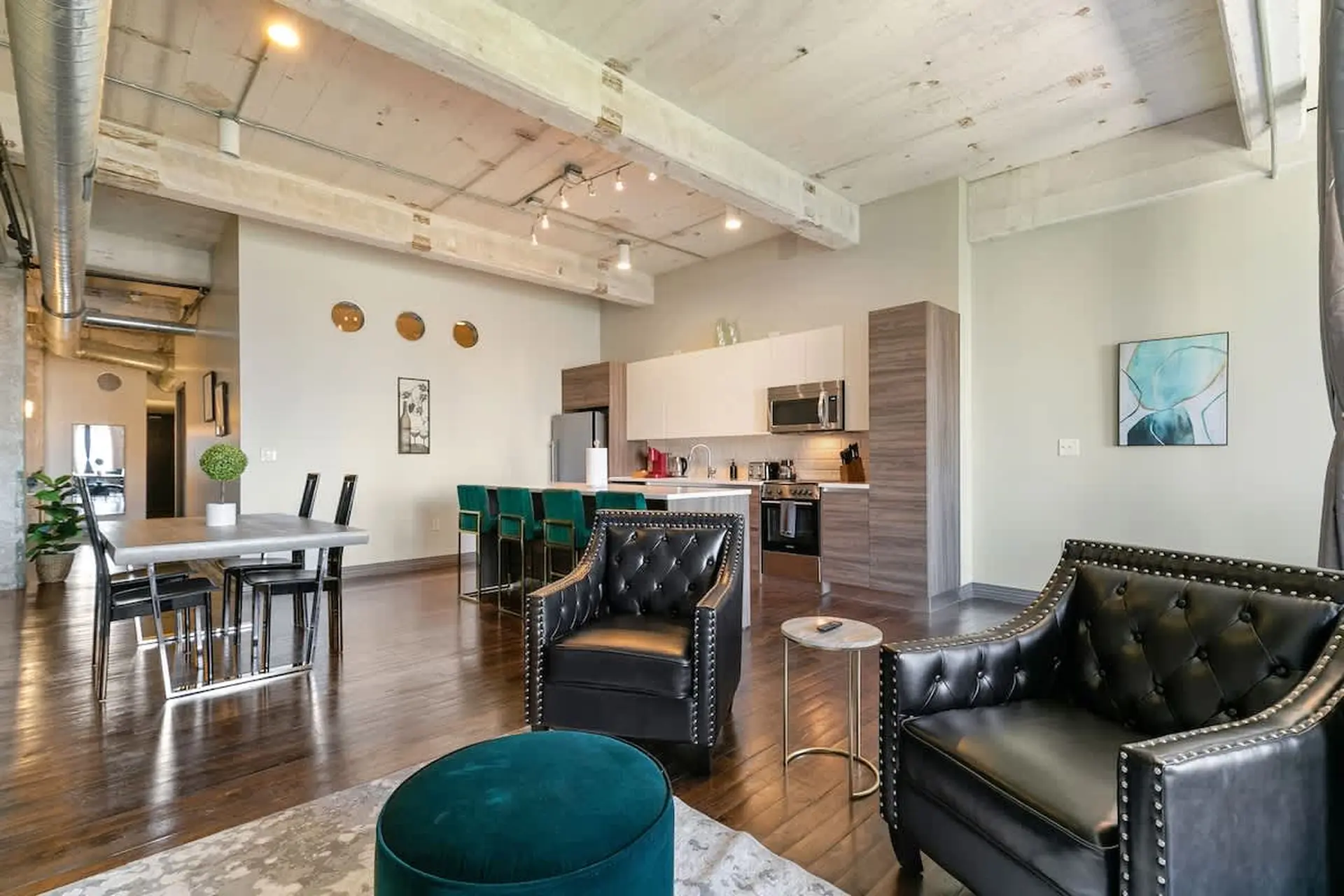 Luxury loft living room and kitchen with industrial beams, dining table, bar stools, and leather arm