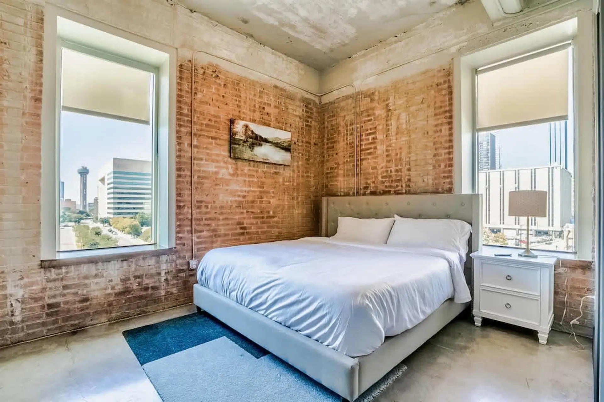 A bedroom with a brick wall, large windows, and a bed.