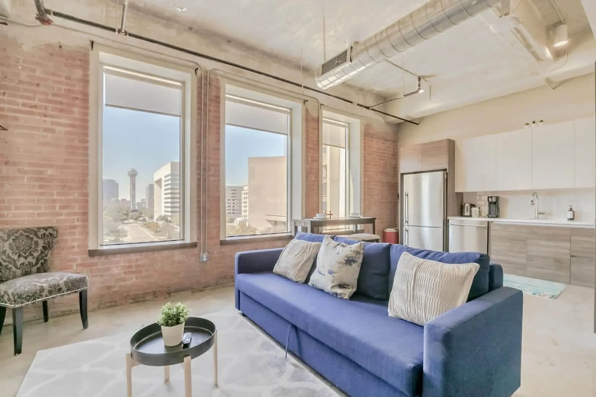 A blue couch with pillows sits in front of a window with a city view.
