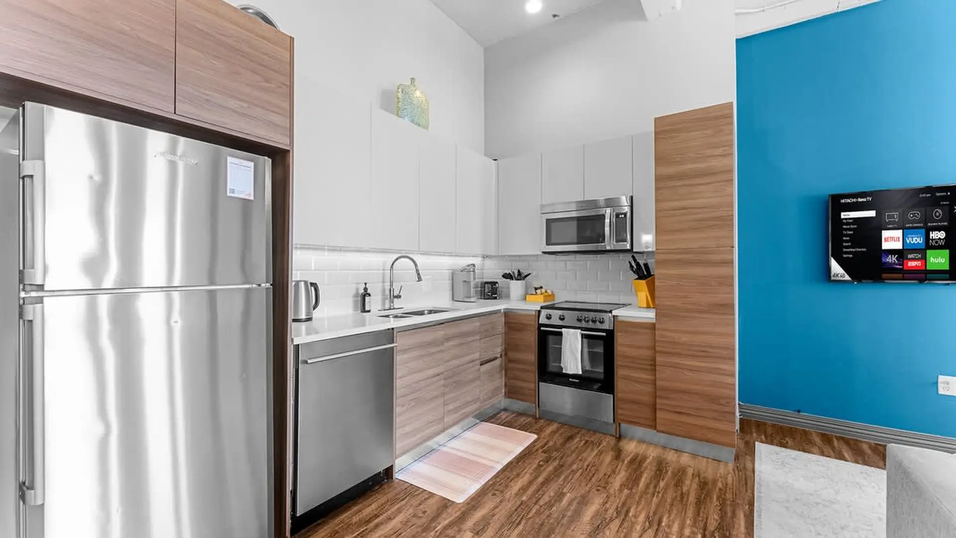 A modern kitchen with a stainless steel refrigerator and appliances, wood cabinets, and a blue wall 